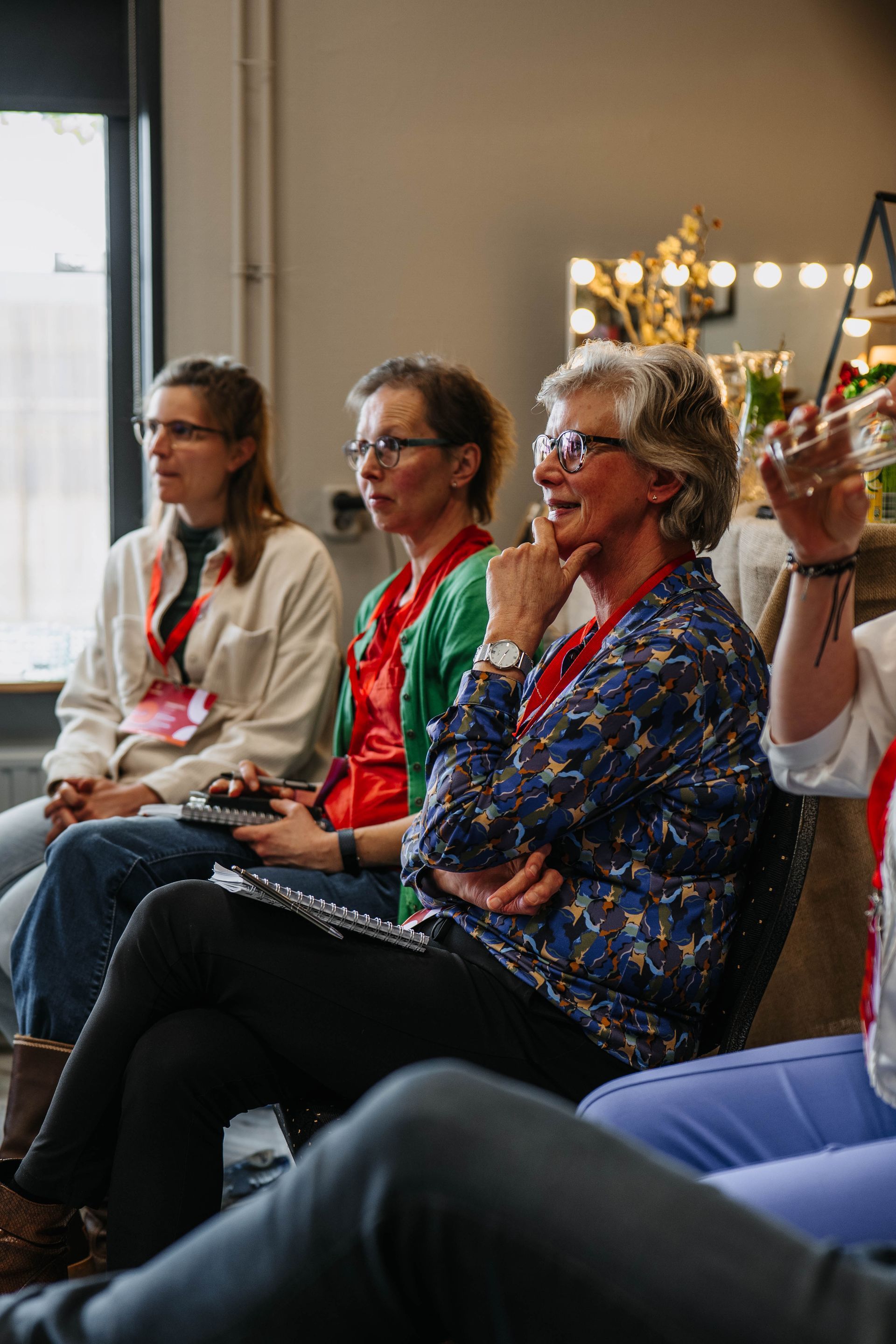 Drie mensen zitten in een goed verlichte ruimte en kijken aandachtig voor zich uit tijdens een groepsactiviteit of presentatie.