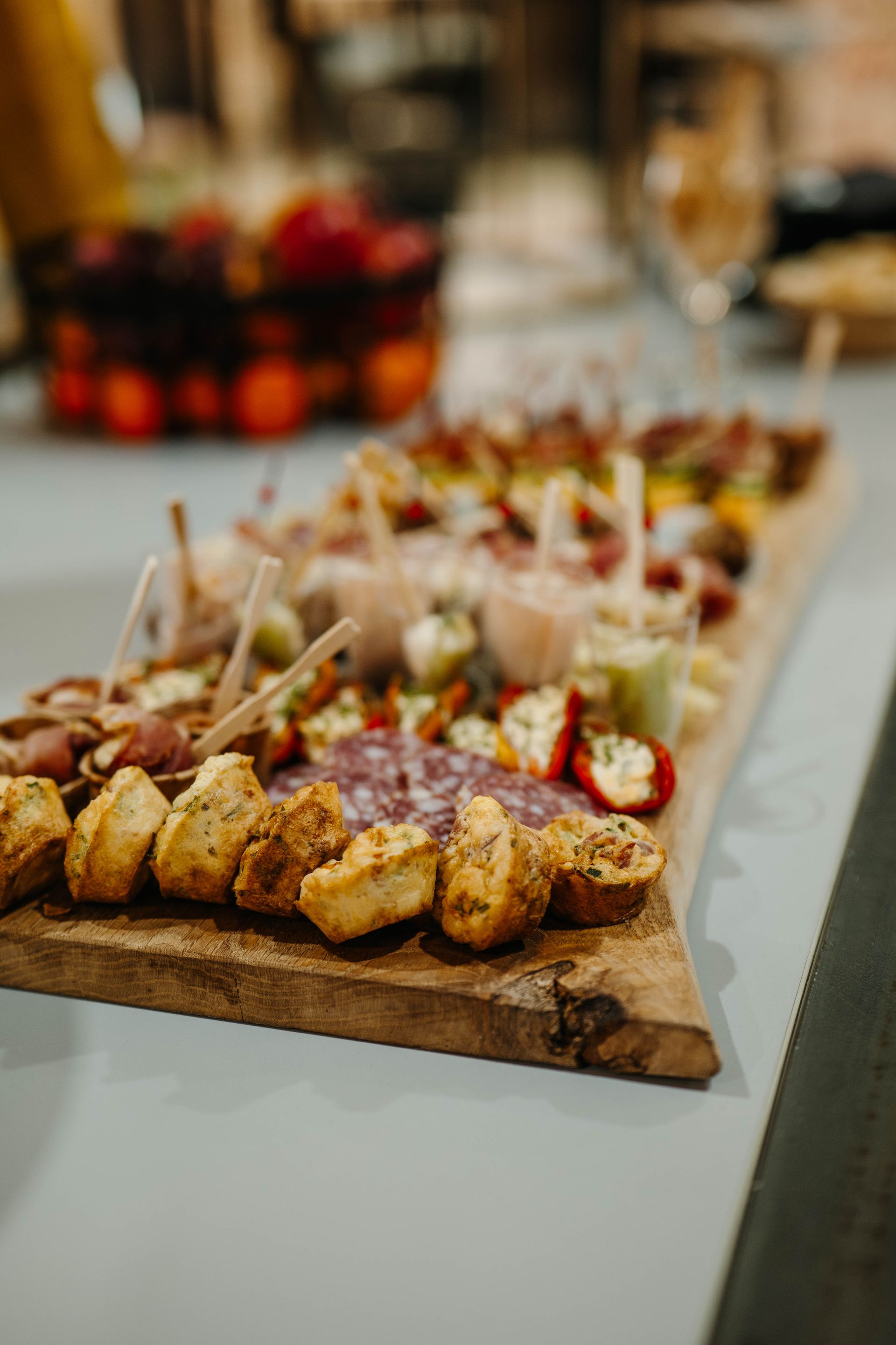 Een houten serveerplank met daarop een assortiment kleine hapjes, muffins en plakjes vleeswaren op een feestje.
