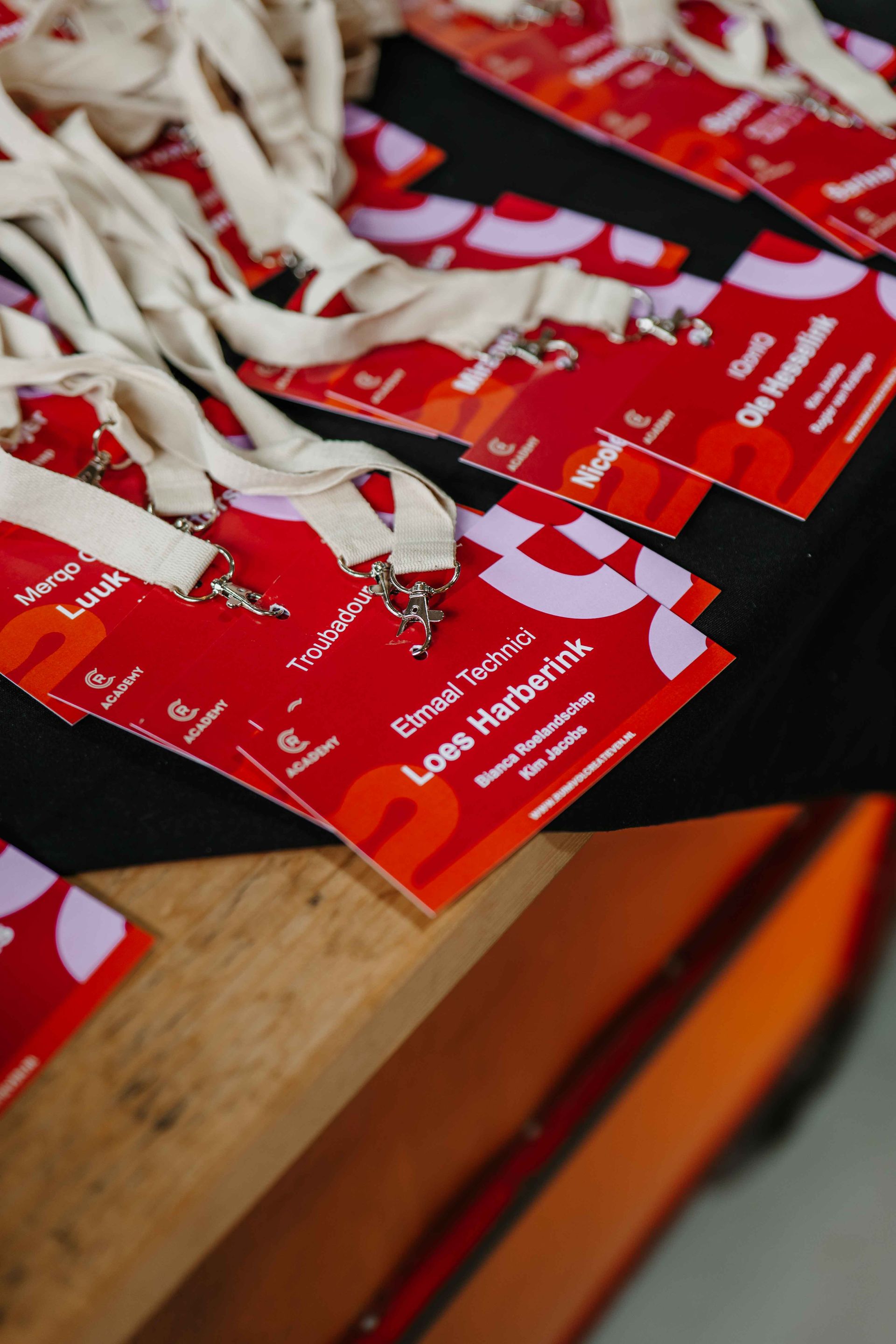 Een stapel rood-witte evenementkoordjes met daarop gedrukte namen van deelnemers ligt op een houten ondergrond.