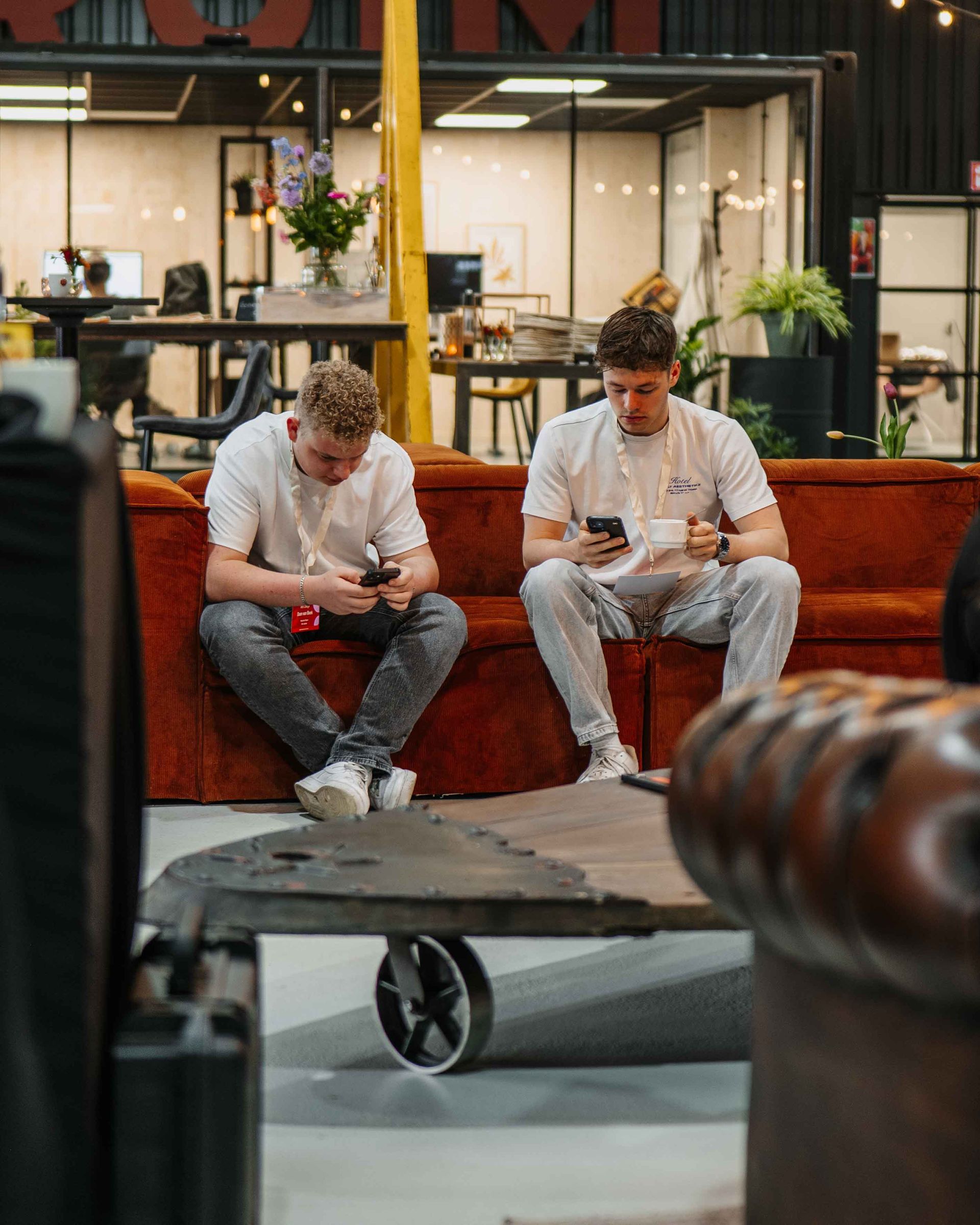 Twee mensen zitten op een roestbruine bank in een kantoor en kijken naar hun smartphones.
