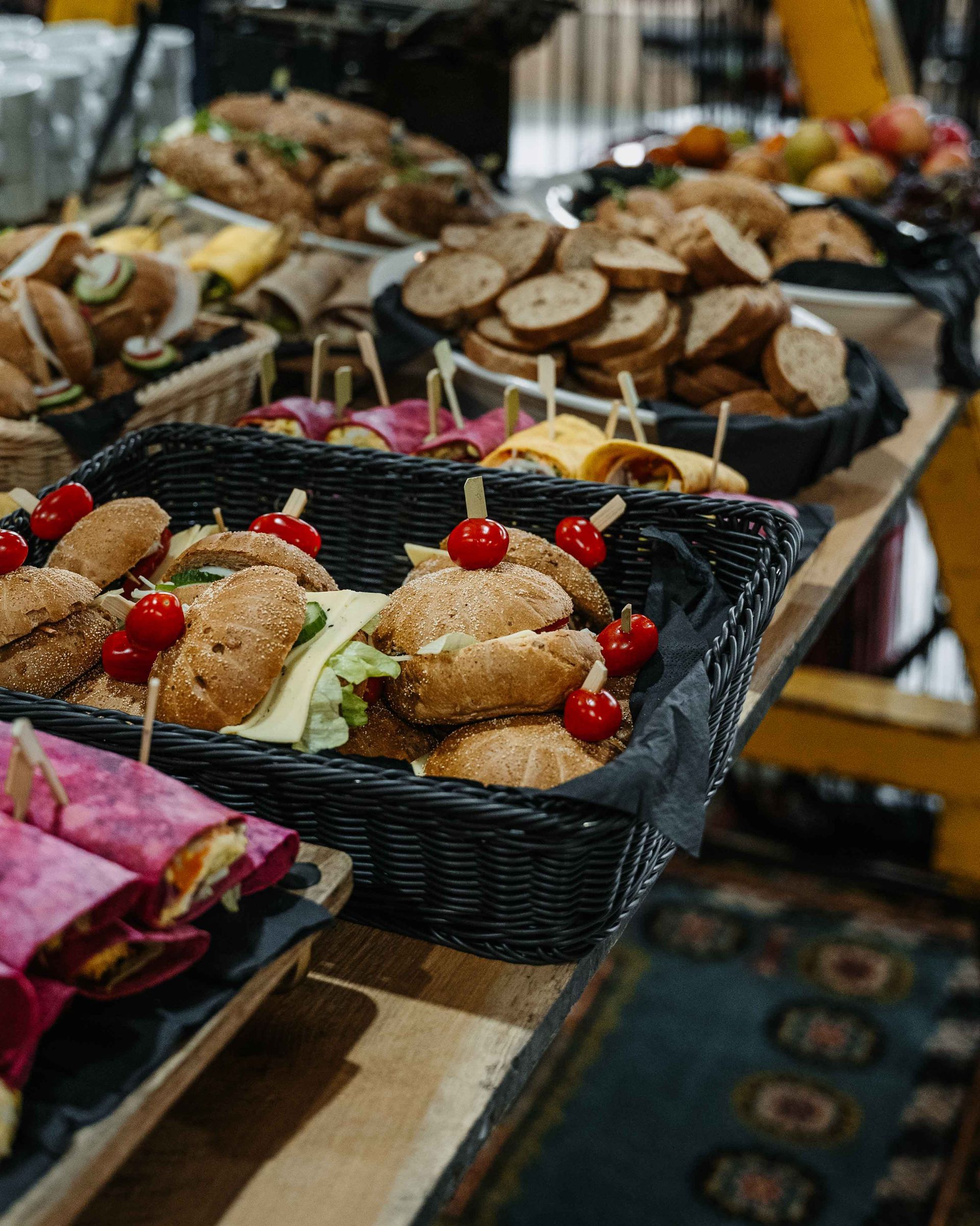 Een tafel vol manden met diverse sandwiches, broodjes, wraps en gesneden brood bij een cateringevenement.