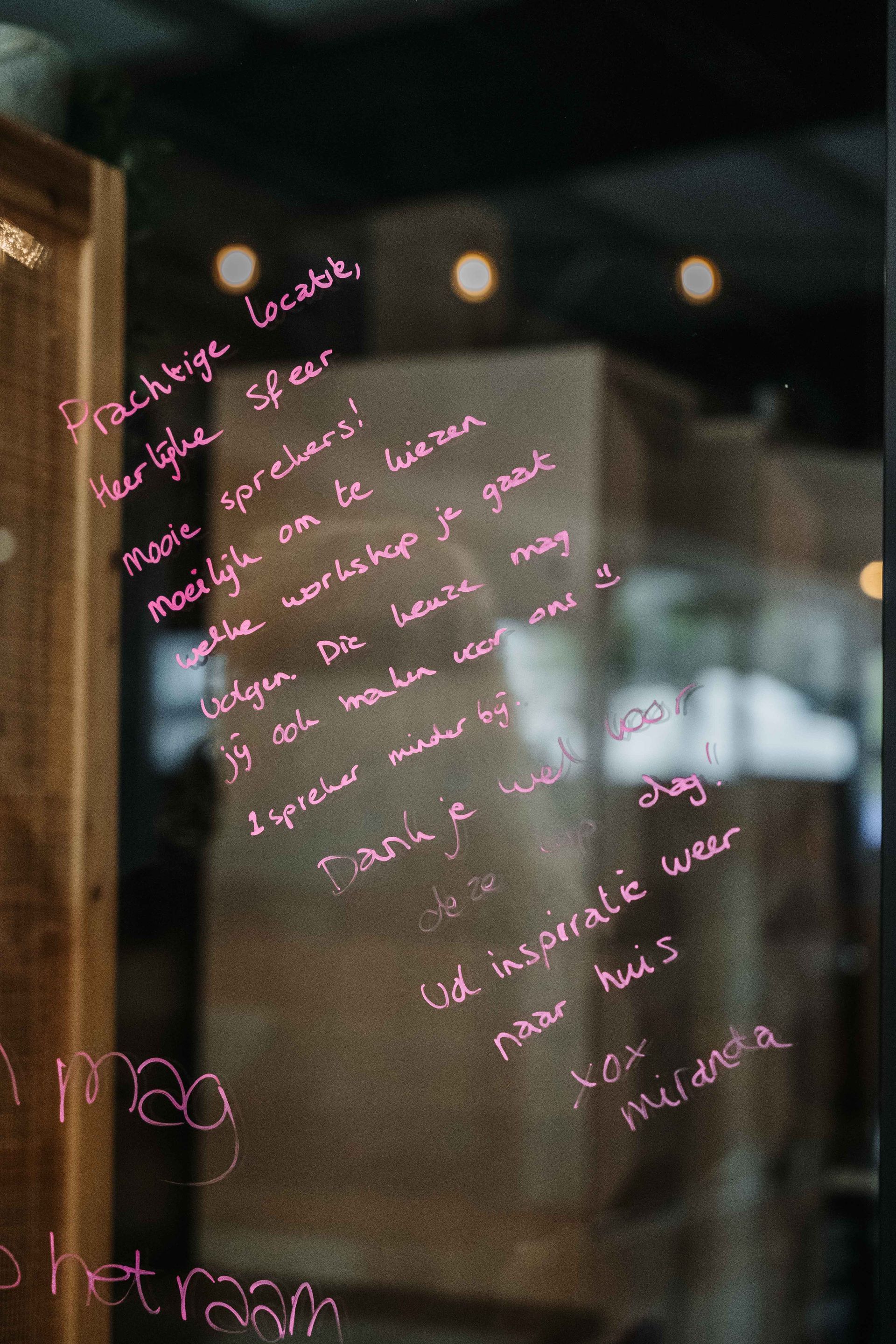 Een handgeschreven roze boodschap op een glazen deur, waarin de locatie, de sfeer en de workshop worden geprezen, ondertekend door Maranda.