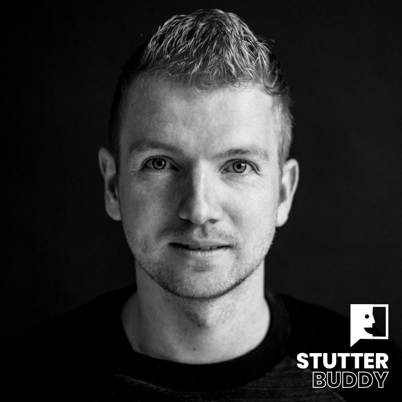 Een zwart-wit portretfoto van een persoon tegen een donkere achtergrond met het Stutter Buddy-logo in de rechterbenedenhoek.