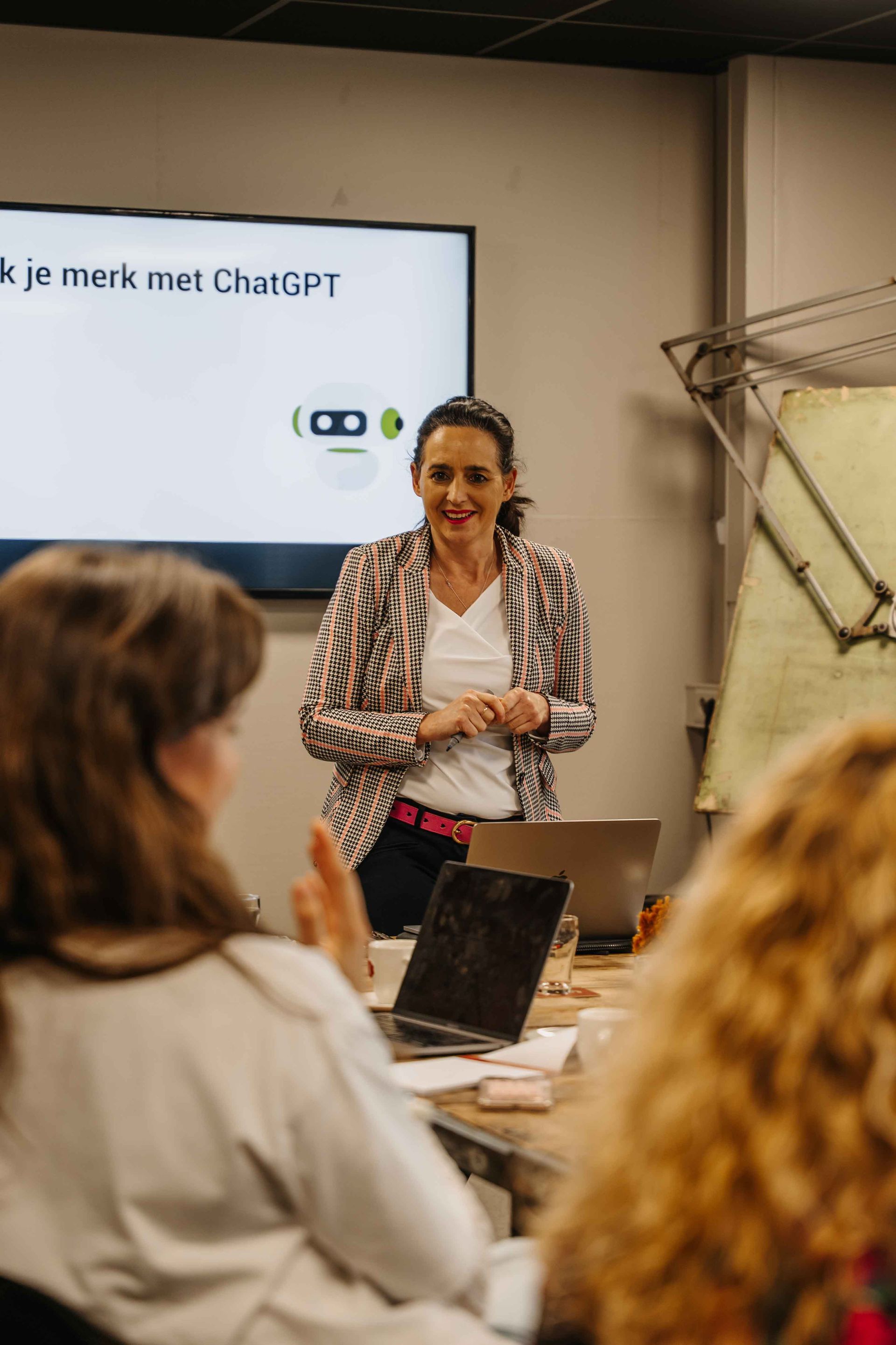 Een presentator spreekt voor een scherm waarop het ChatGPT-logo en tekst worden weergegeven, en richt zich tot een publiek in een kantooromgeving.