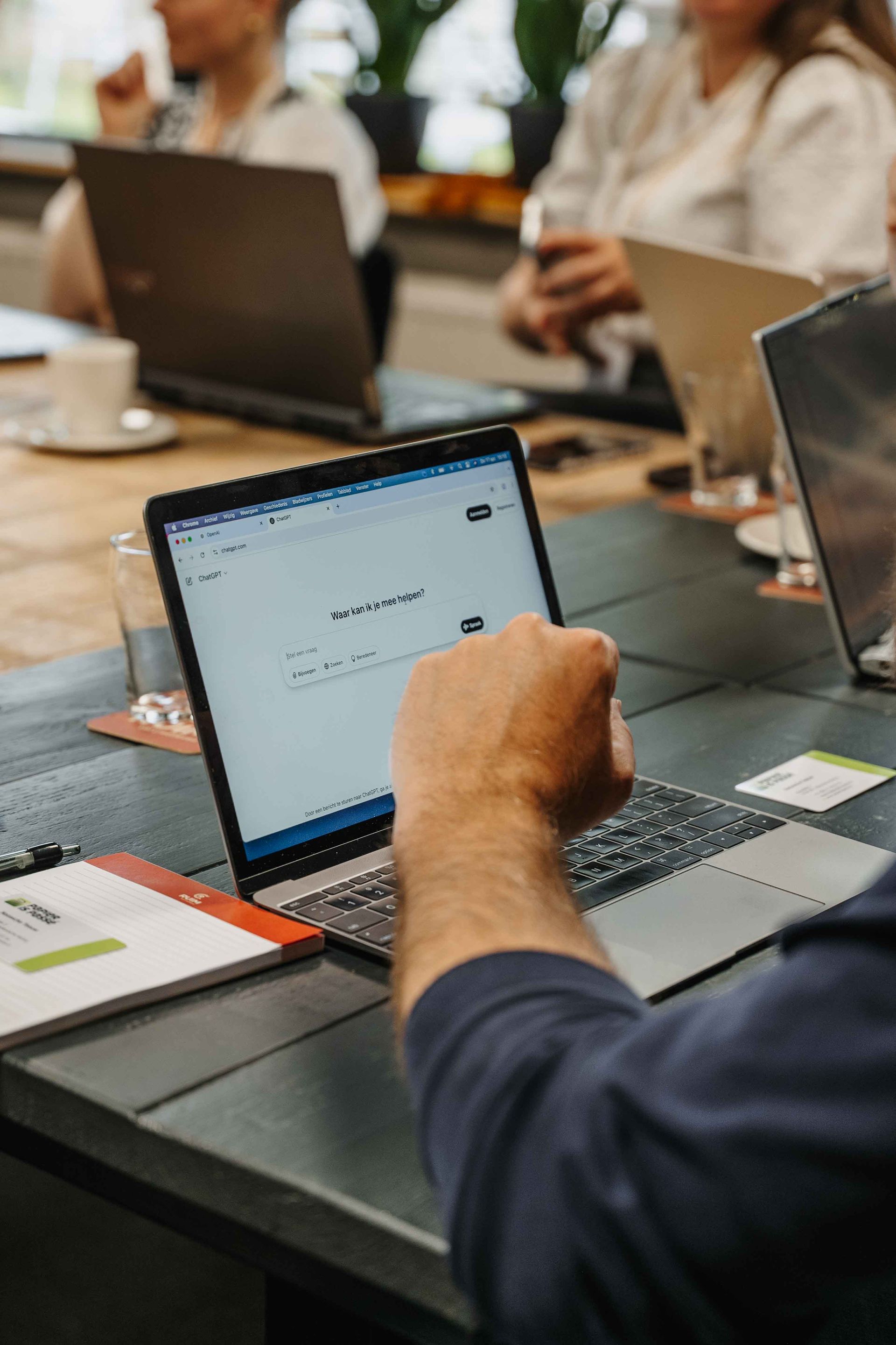 Tijdens een vergadering met collega's werkt iemand aan een laptop aan een tafel.