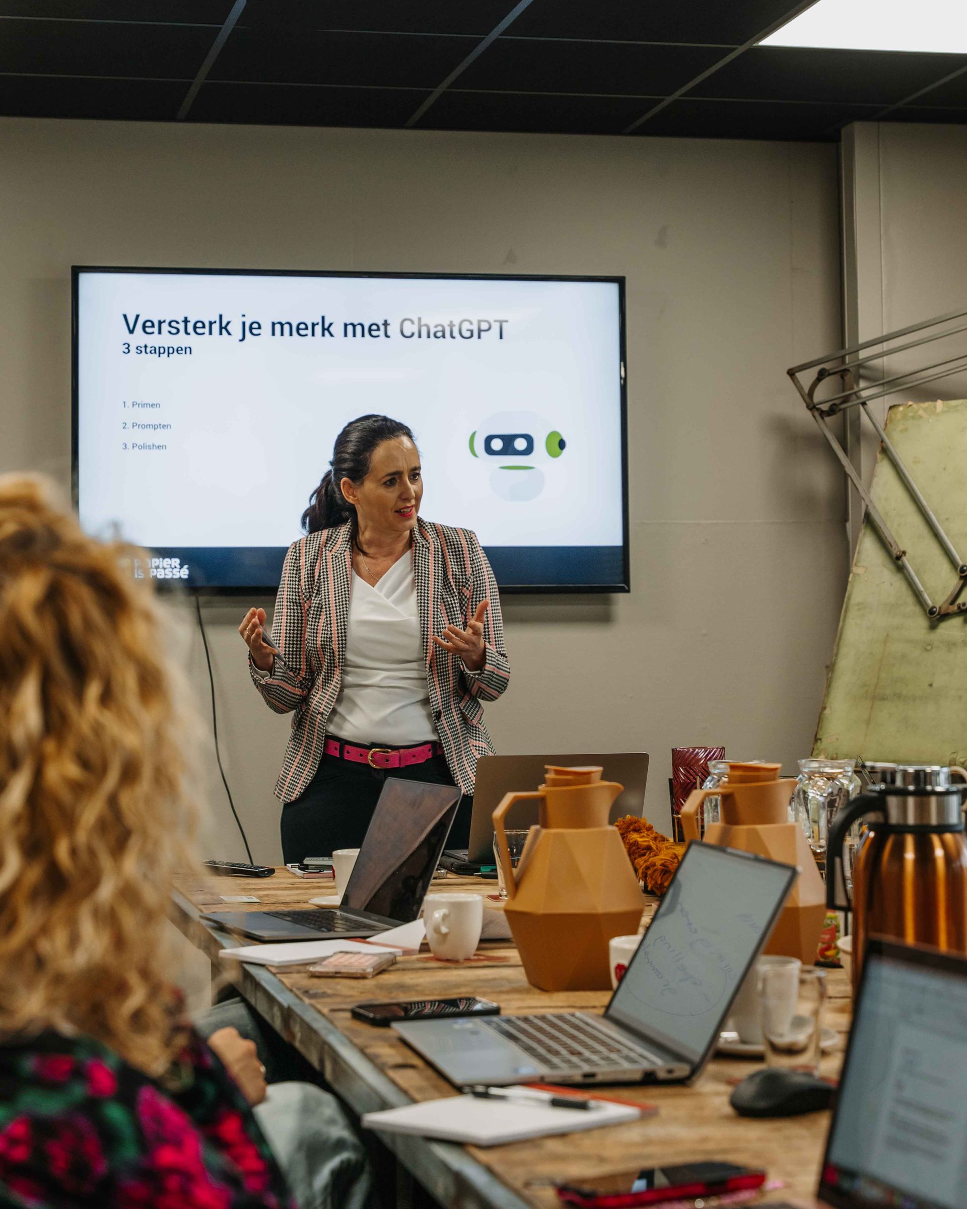 Een presentator staat voor een scherm waarop 