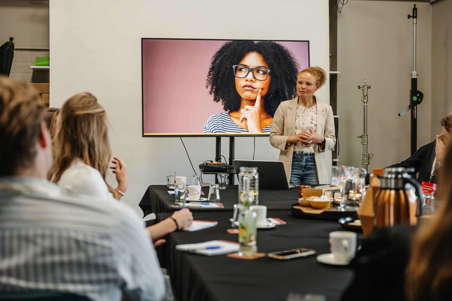 Een spreker geeft een presentatie aan een zittend publiek in een vergaderzaal, met achter haar een geprojecteerde foto van een denkend persoon.