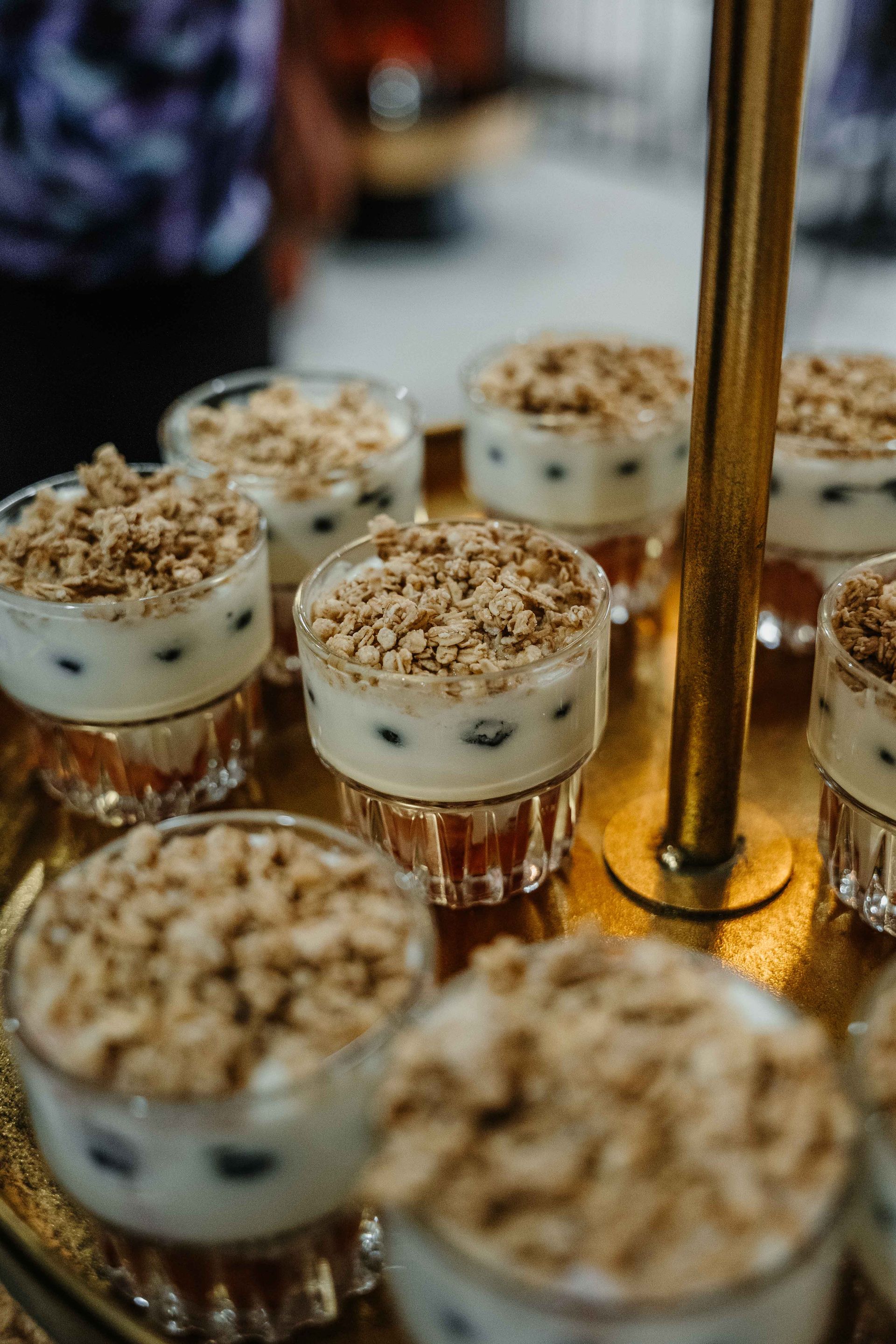 Kleine glazen schaaltjes gevuld met yoghurt, bosbessen en granola, gerangschikt op een goudkleurig metalen dienblad.
