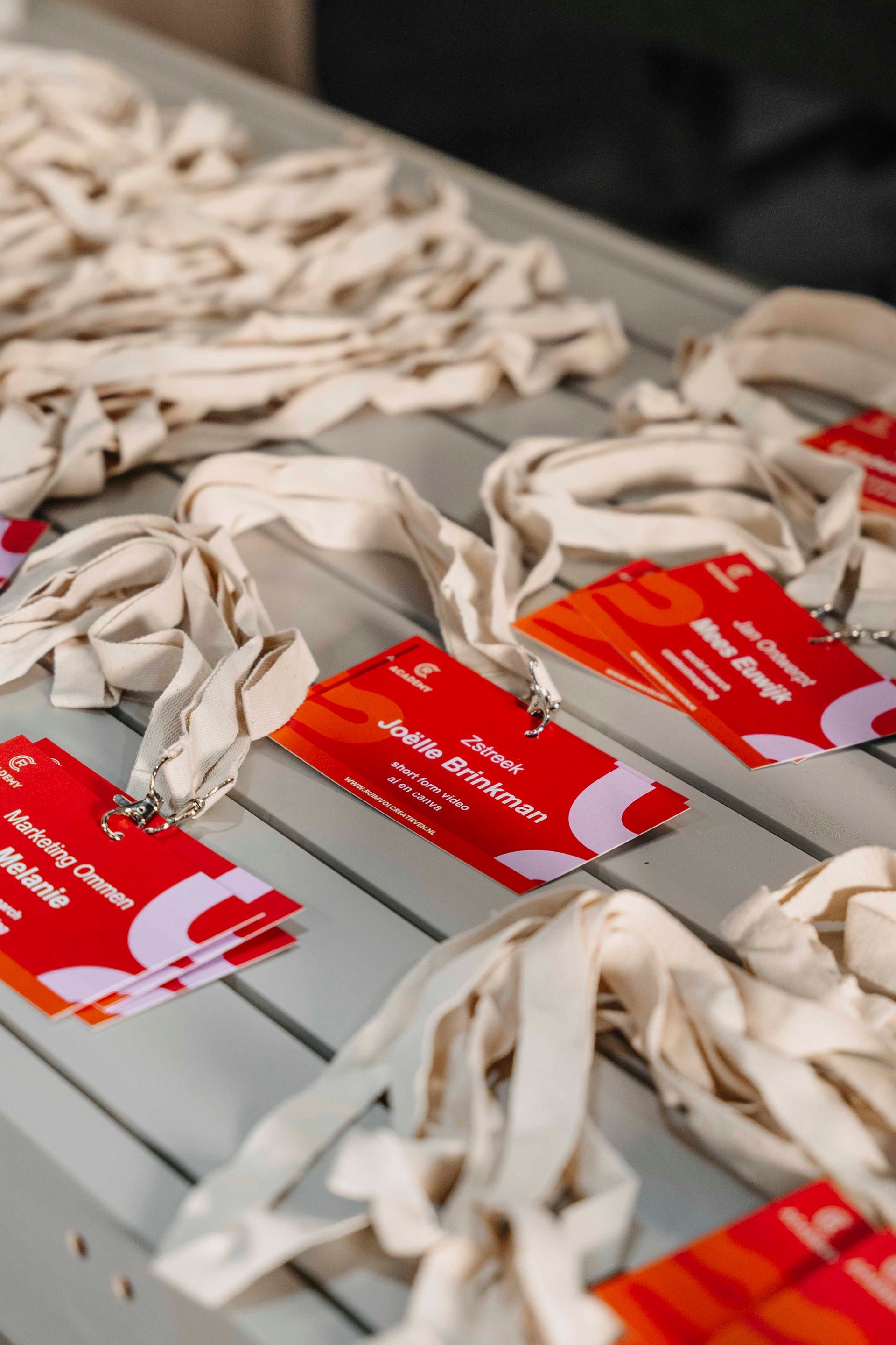 Meerdere rode naamkaartjes voor evenementen, met daaraan bevestigde crèmekleurige keycords, liggen uitgestald op een lichtgrijze tafel.