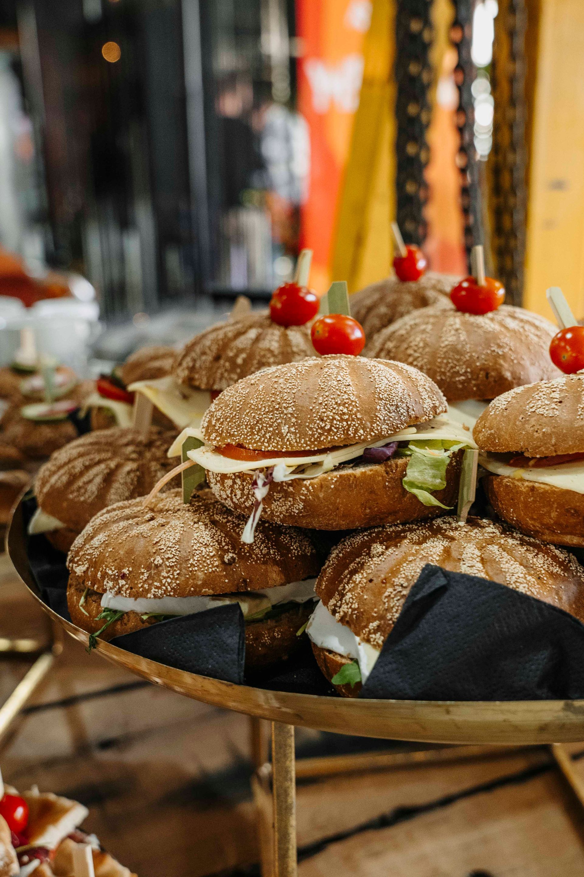 Op een etagère staan ​​verschillende kleine sliders op sesamzaadbroodjes, belegd met cherrytomaatjes aan spiesjes.