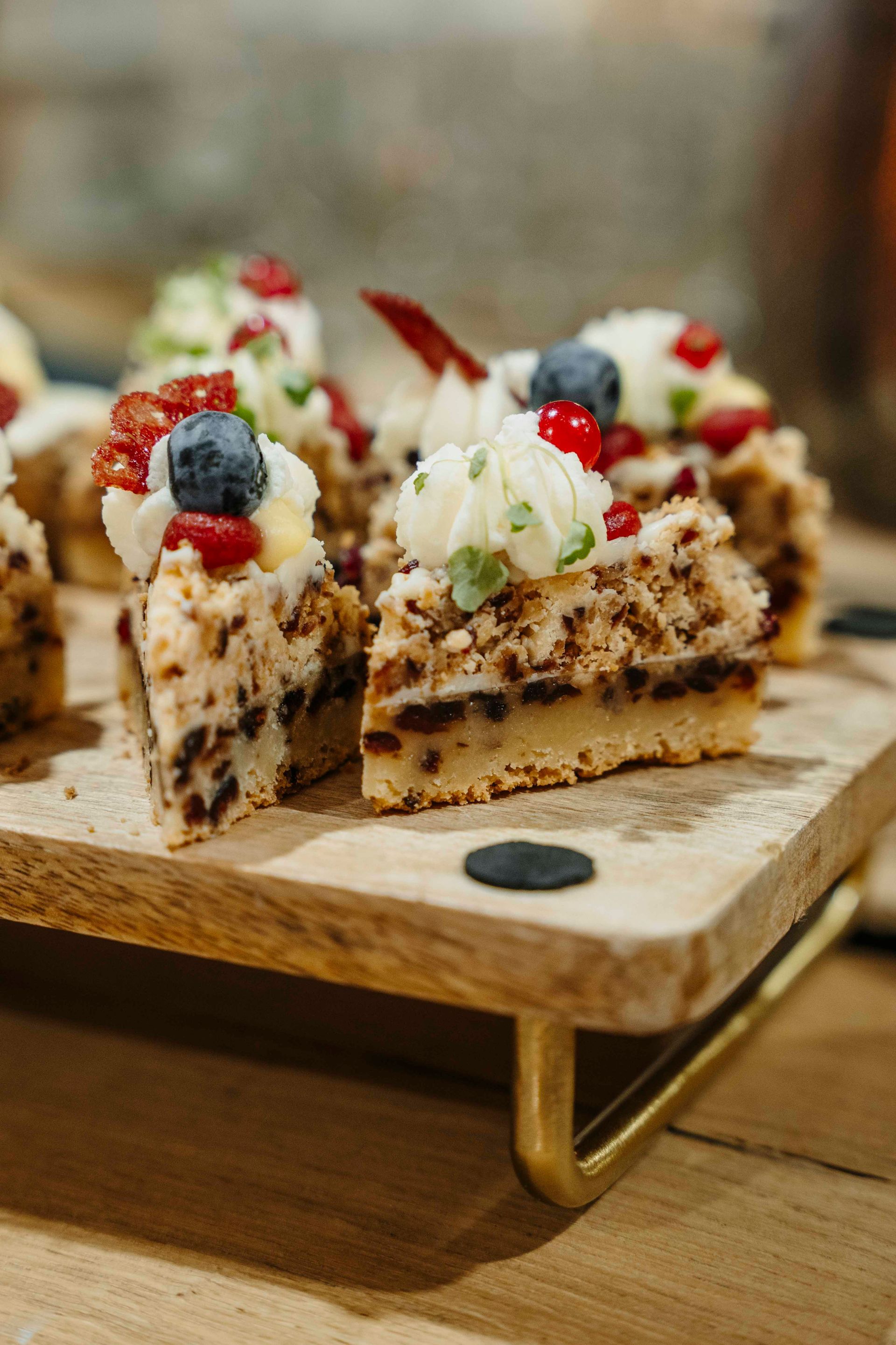 Driehoekige desserthapjes van koekjesdeeg, gegarneerd met slagroom, bosbessen en rode bessen, geserveerd op een houten dienblad.