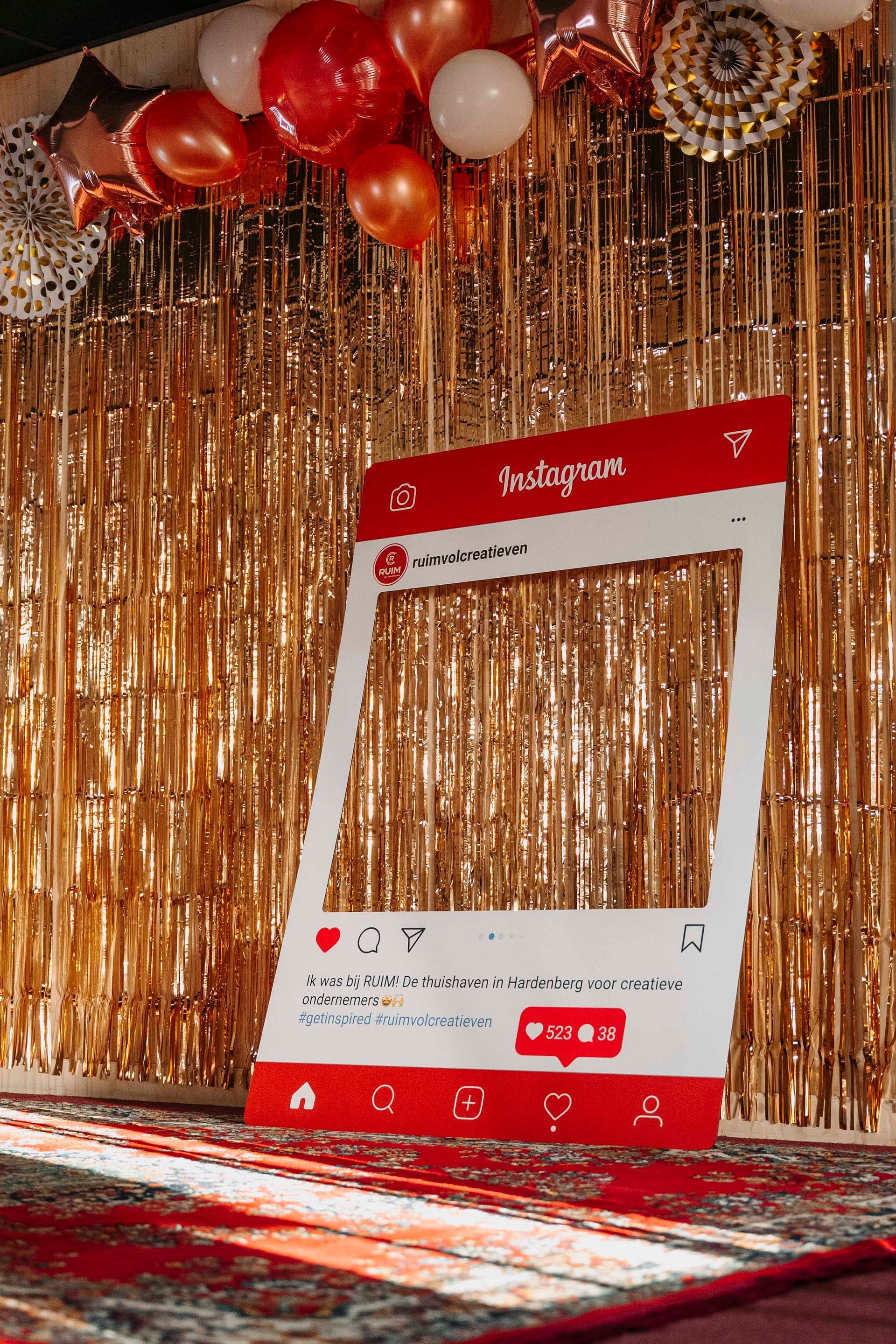 Een fotohokje met een Instagram-thema staat voor een achtergrond van gouden slingers, versierd met rode en witte ballonnen.