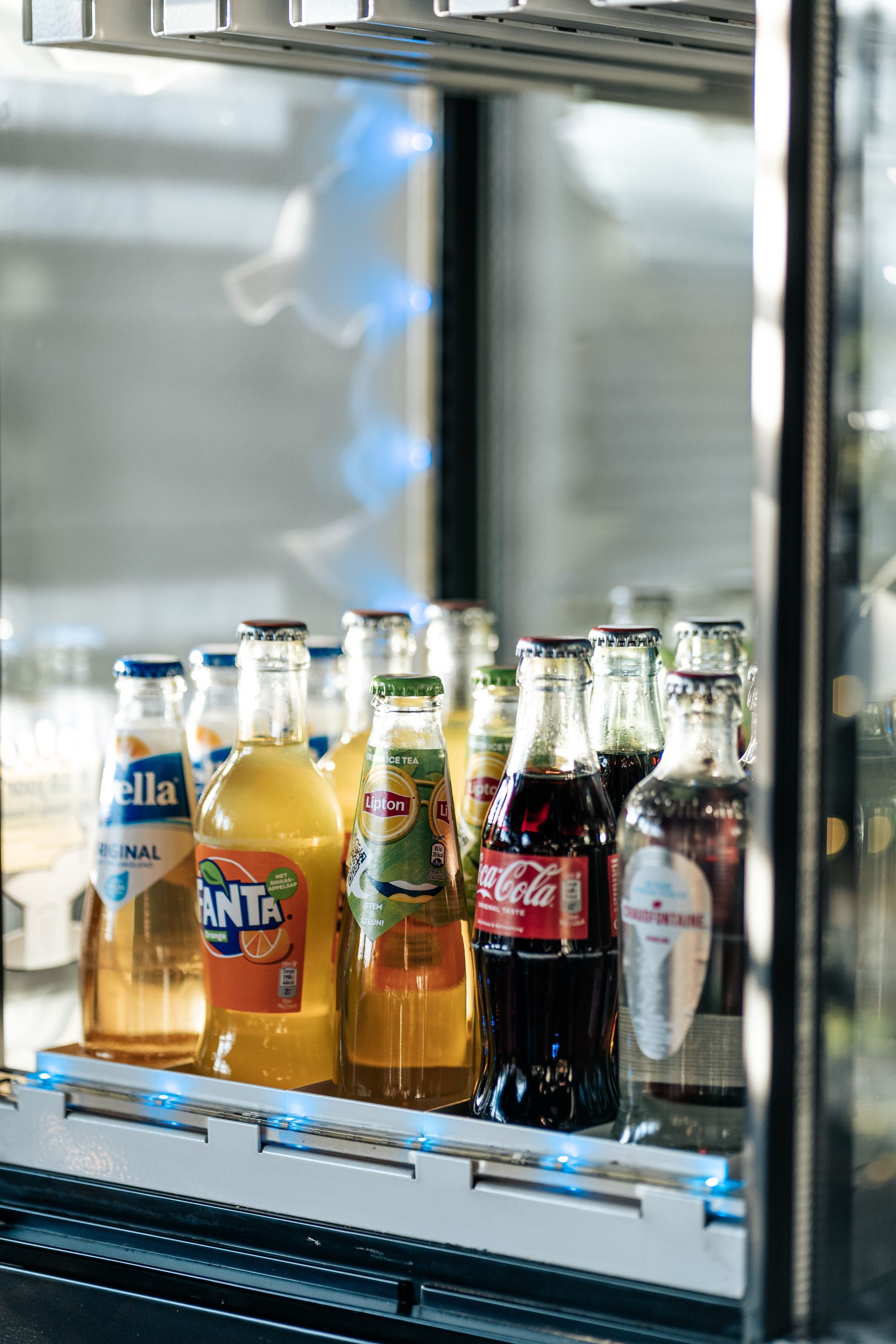 Een koelkast gevuld met flessen frisdrank waaronder fanta en coca cola.