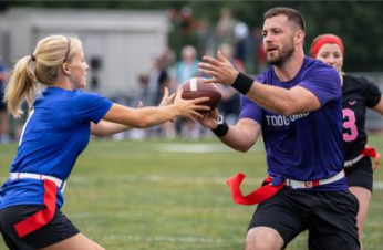 Two flag football players reach for the ball during a game on a grassy field