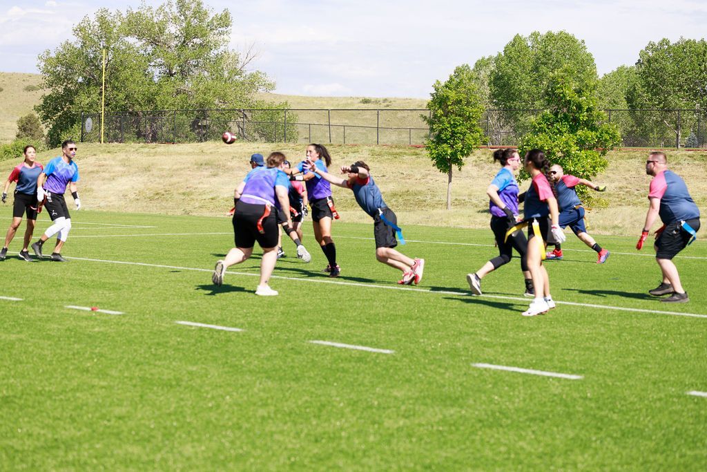 People playing flag football on a grassy field under bright sunlight