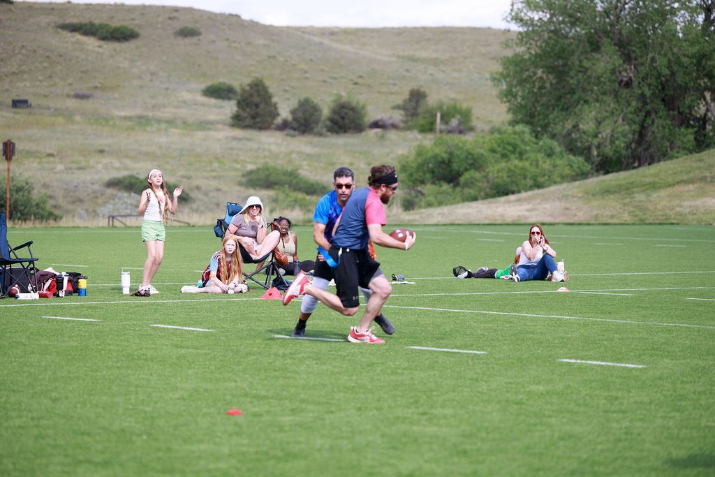 People running on a grassy field during a sports event, with spectators in the background.