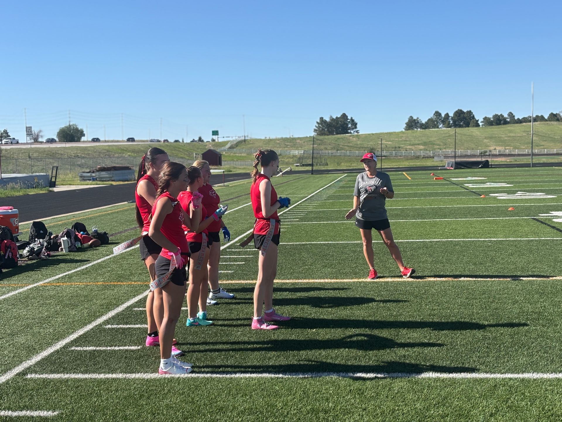 Youth athletes in red and black uniforms standing on a football field under a clear blue sky