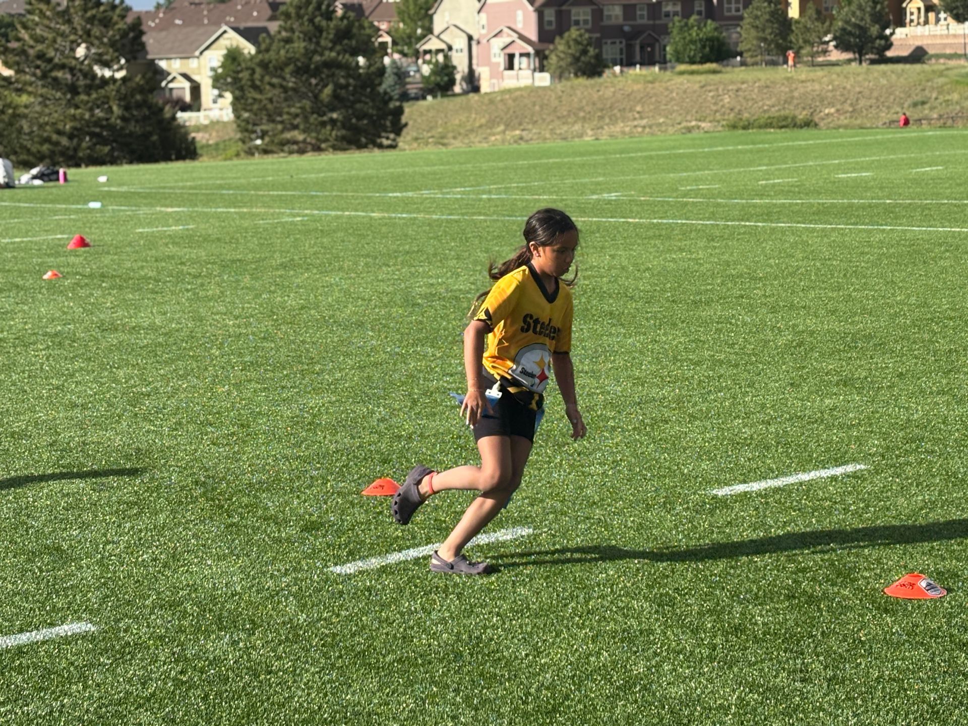 Youth athlete in black and yellow jersey running on a grassy field between orange cones