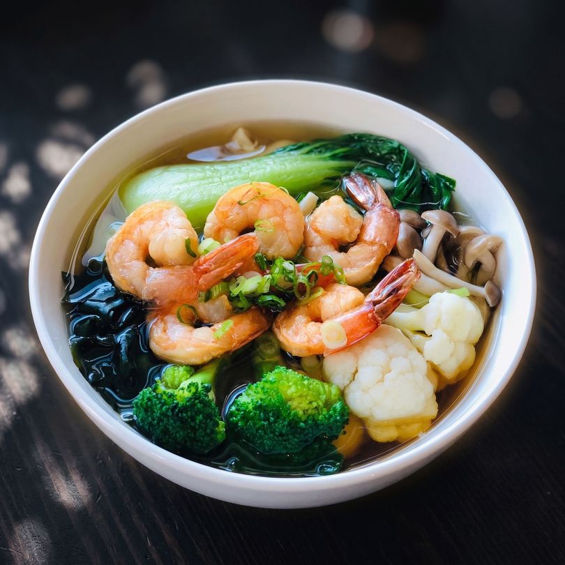 Bowl of shrimp with broccoli, cauliflower, bok choy, and noodles in broth