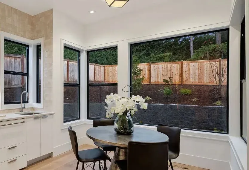 A dining room with a table and chairs and a vase of flowers.