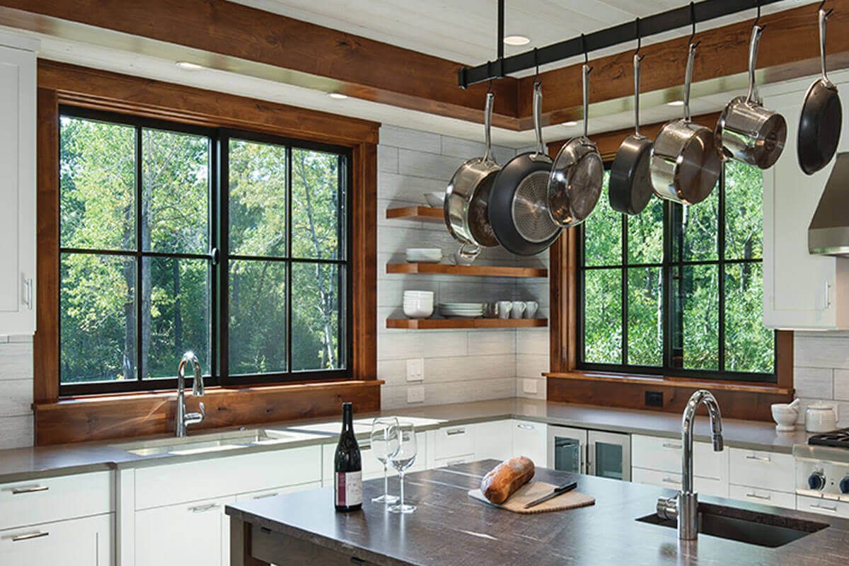 A kitchen with pots and pans hanging from the ceiling and a bottle of wine on the counter.