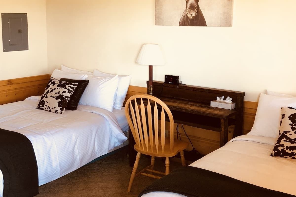 Two beds in a room with a desk and horse picture above. Beds have black blankets and cow print pillows.