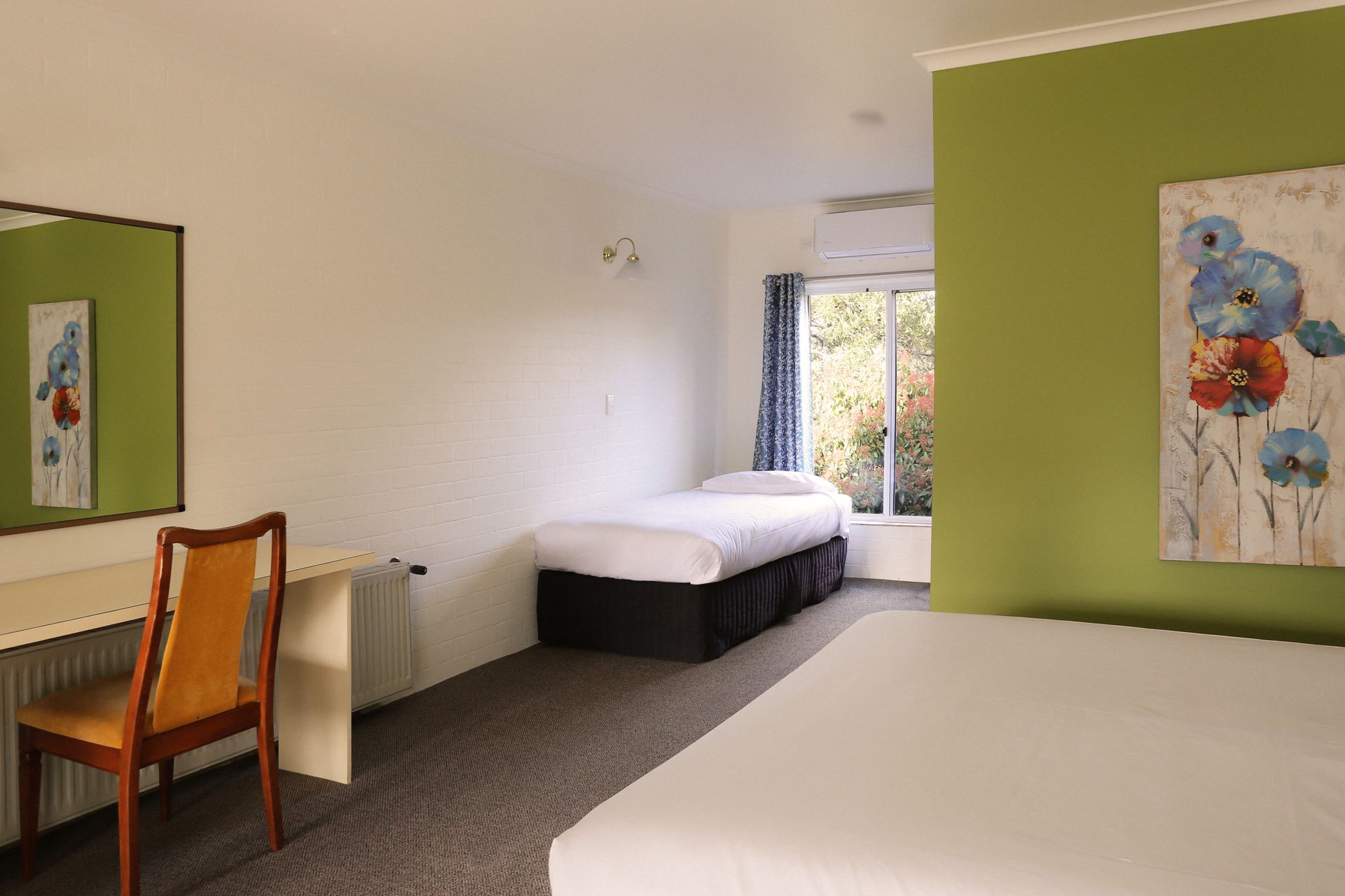 Bedroom with bed, green accent wall, floral artwork, and a window.