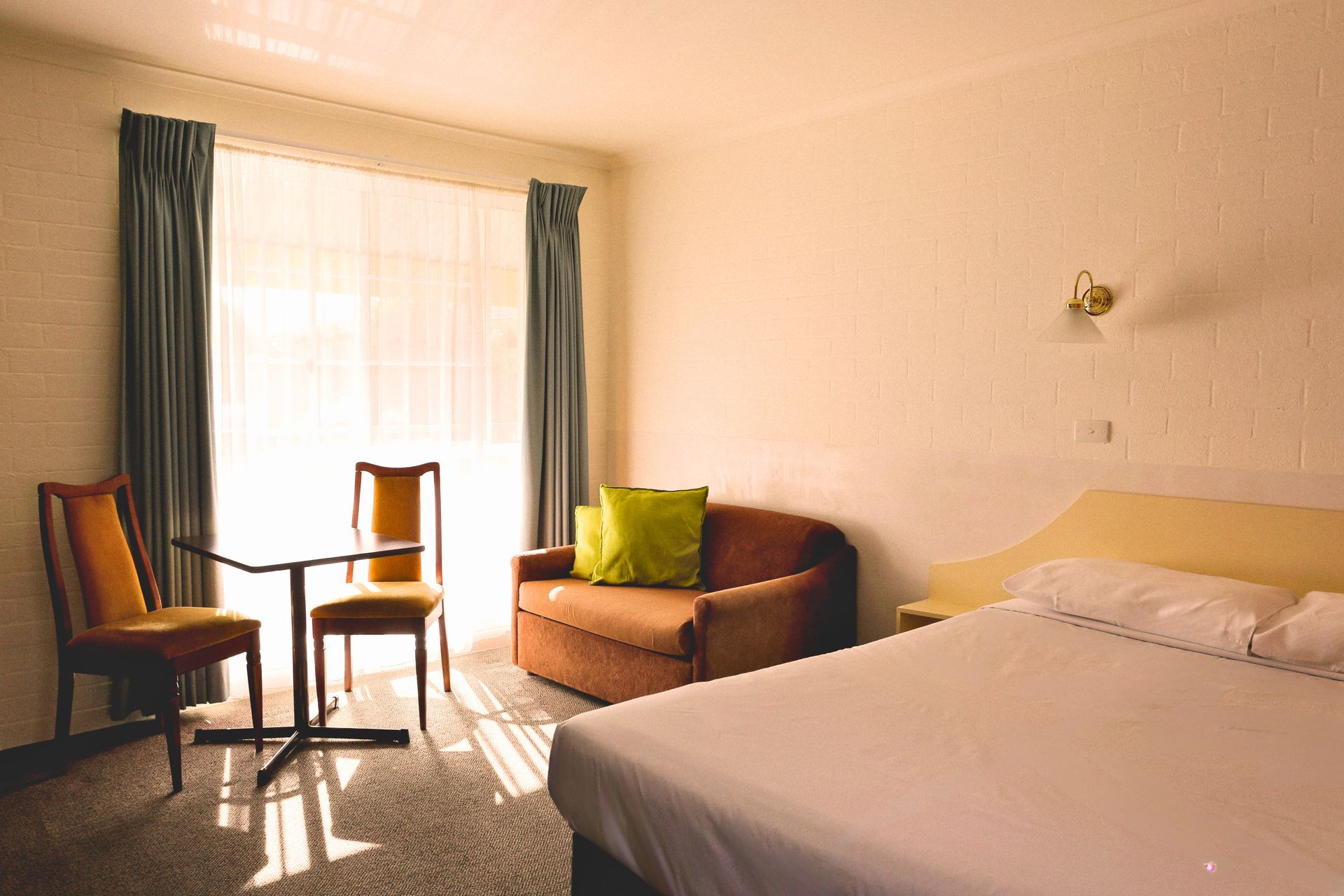 Hotel room with bed, sofa, table, chairs, and window with curtains; neutral color scheme.