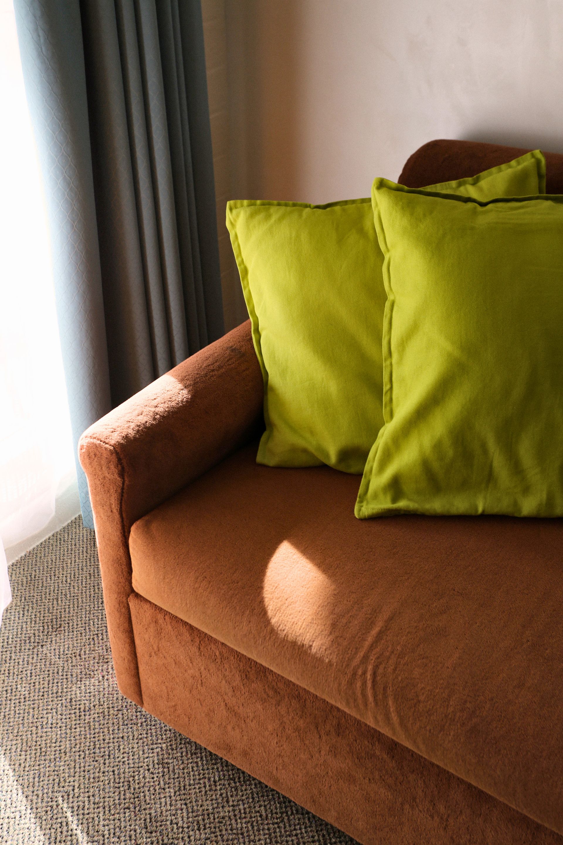 Brown sofa with two lime green pillows near a window with gray curtains.