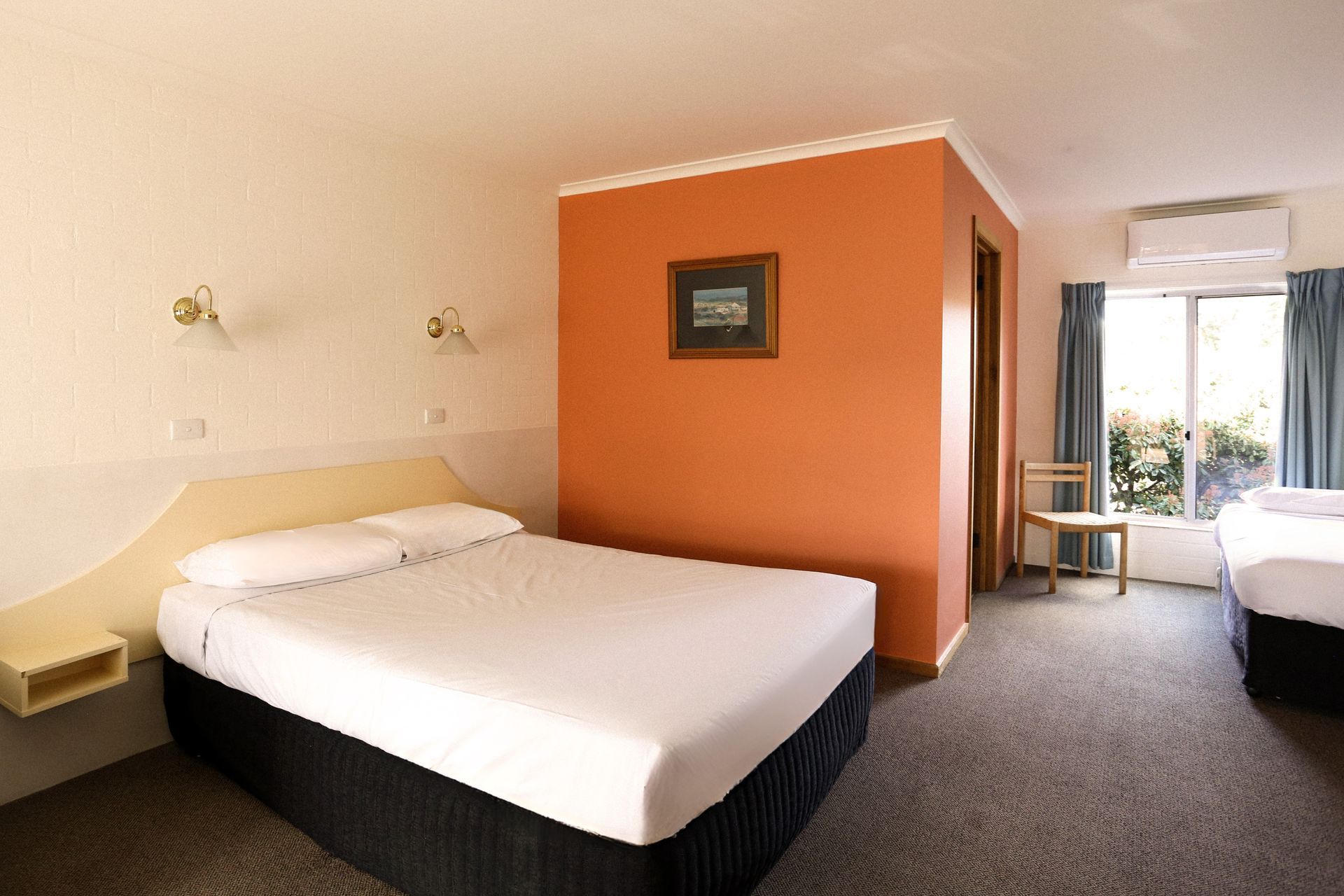 Hotel room with two beds, orange accent wall, and a window.
