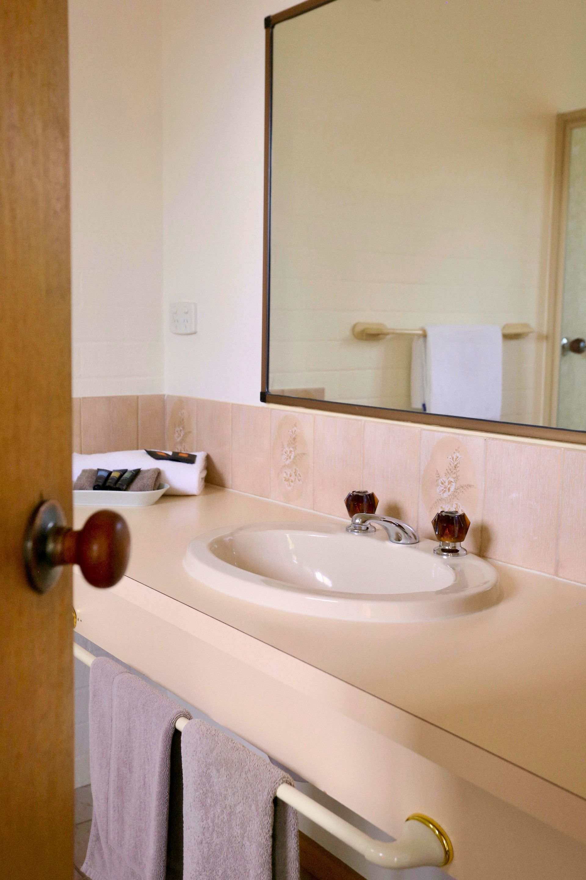 Bathroom sink with beige counter, mirror, and towel rack. Door with doorknob on the left.