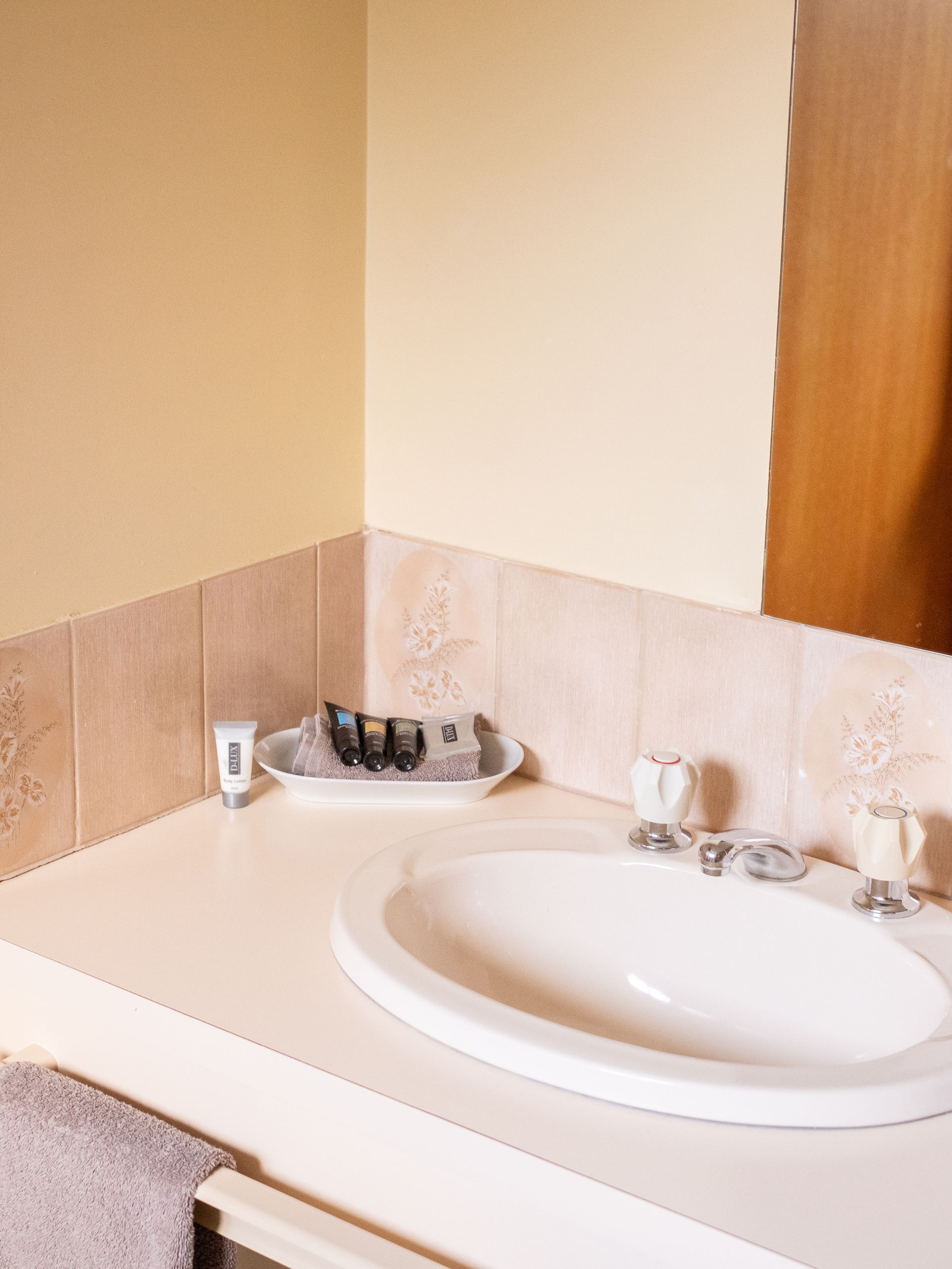 Bathroom vanity with oval sink, toiletries on a tray, beige walls and tile, and a partially visible mirror.