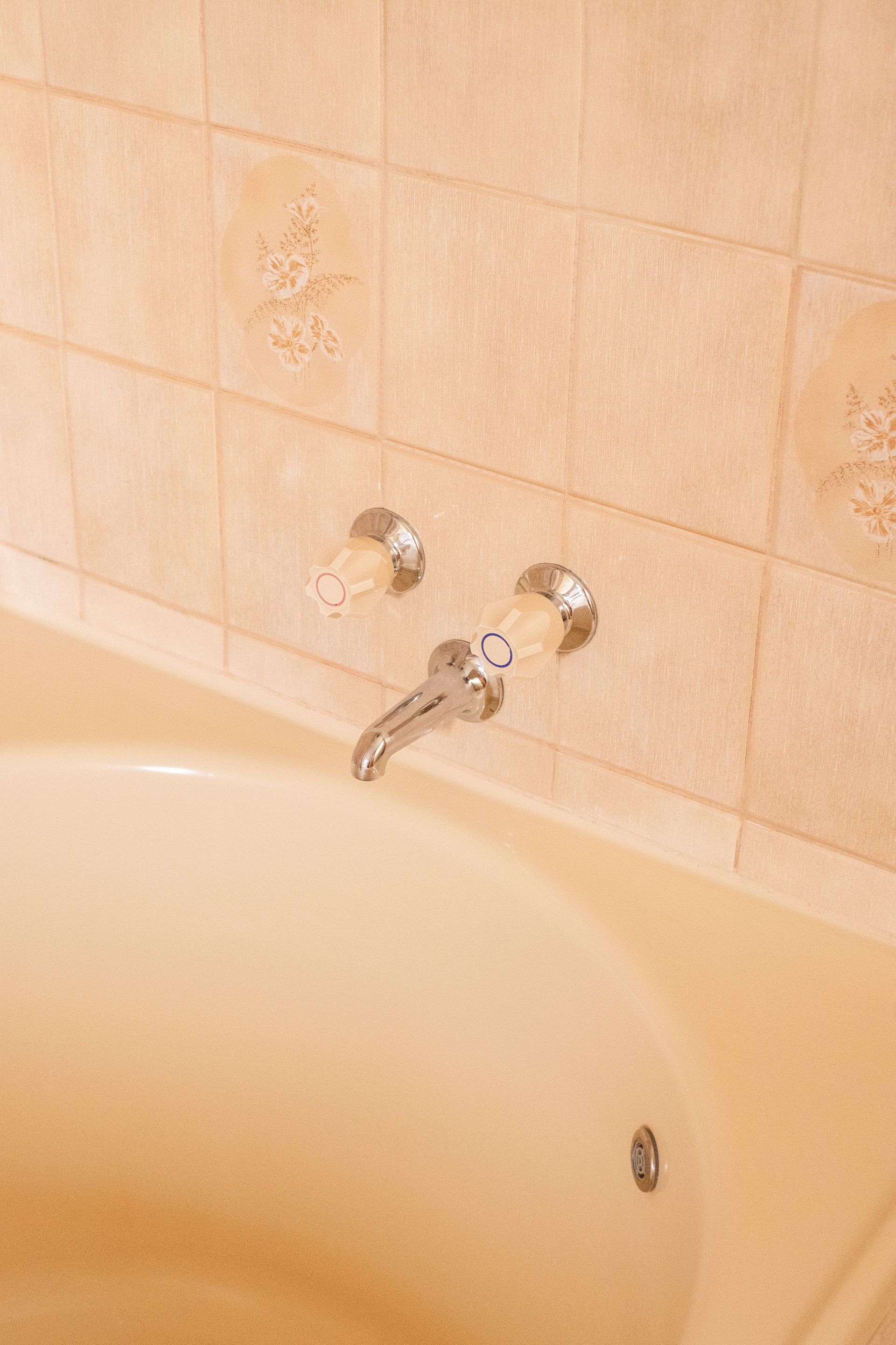 Bathtub with chrome faucet and handles against tan tiled wall.