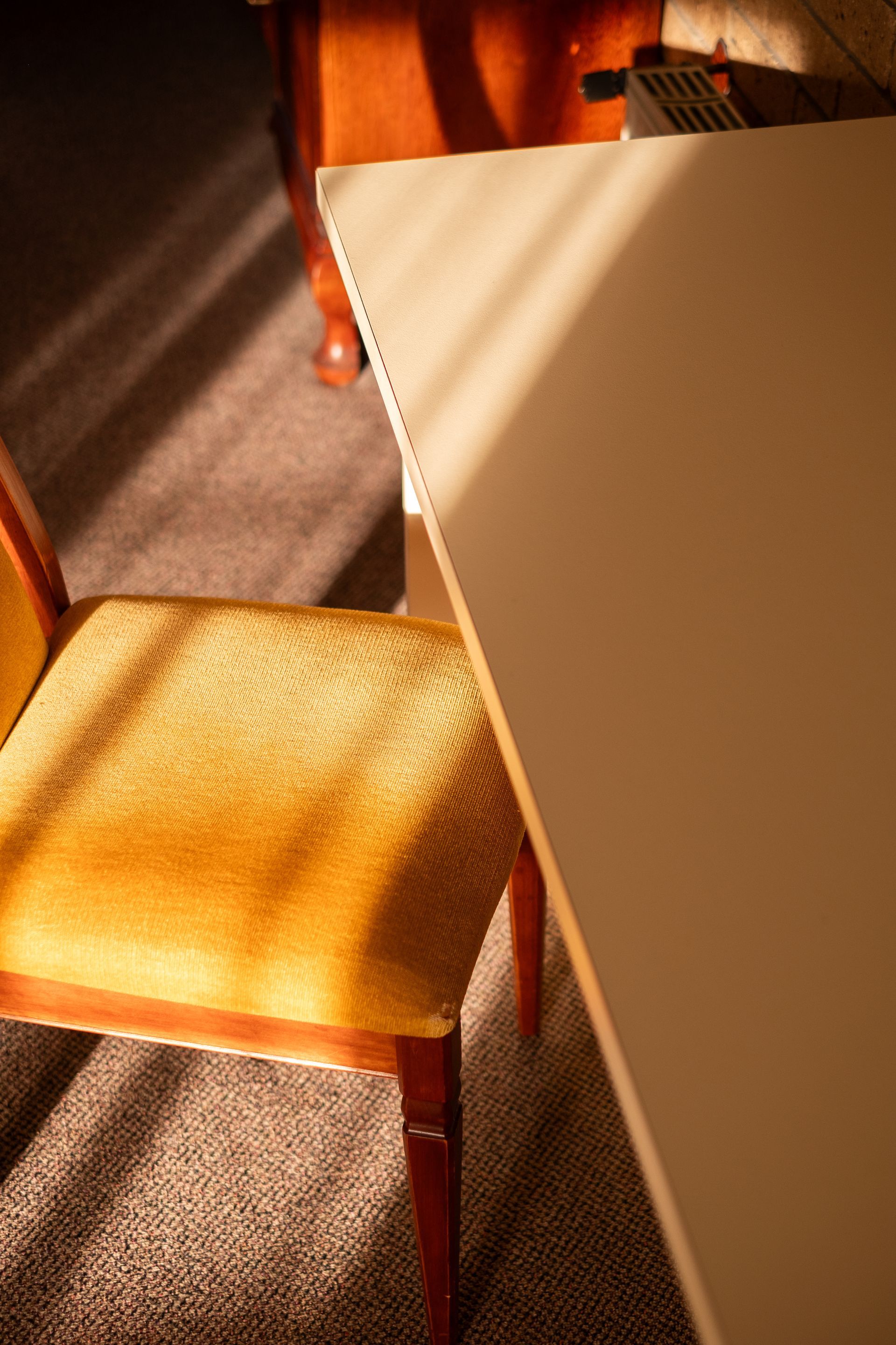 Yellow upholstered chair, white table corner, and wooden furniture under warm sunlight.