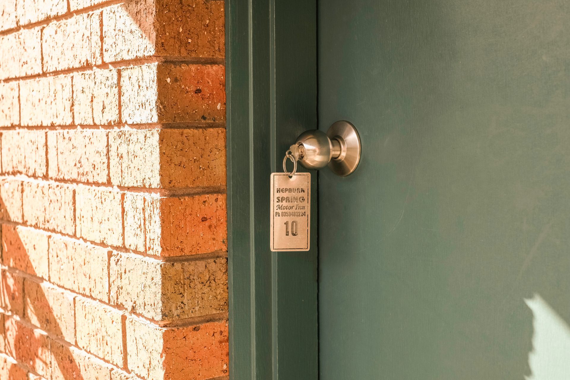 Green door with silver doorknob and a room key. Brick wall on the left.