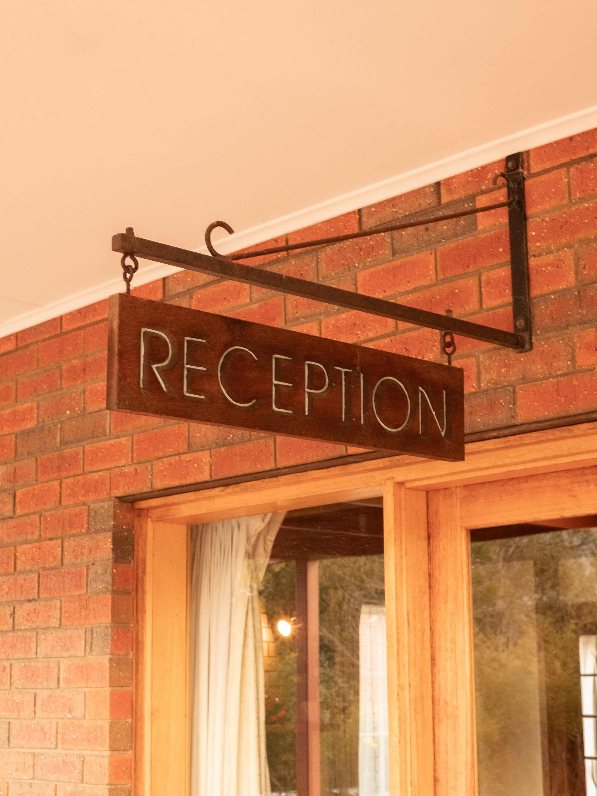 Reception sign hanging from a dark metal bracket, mounted on a brick wall above a wooden door.