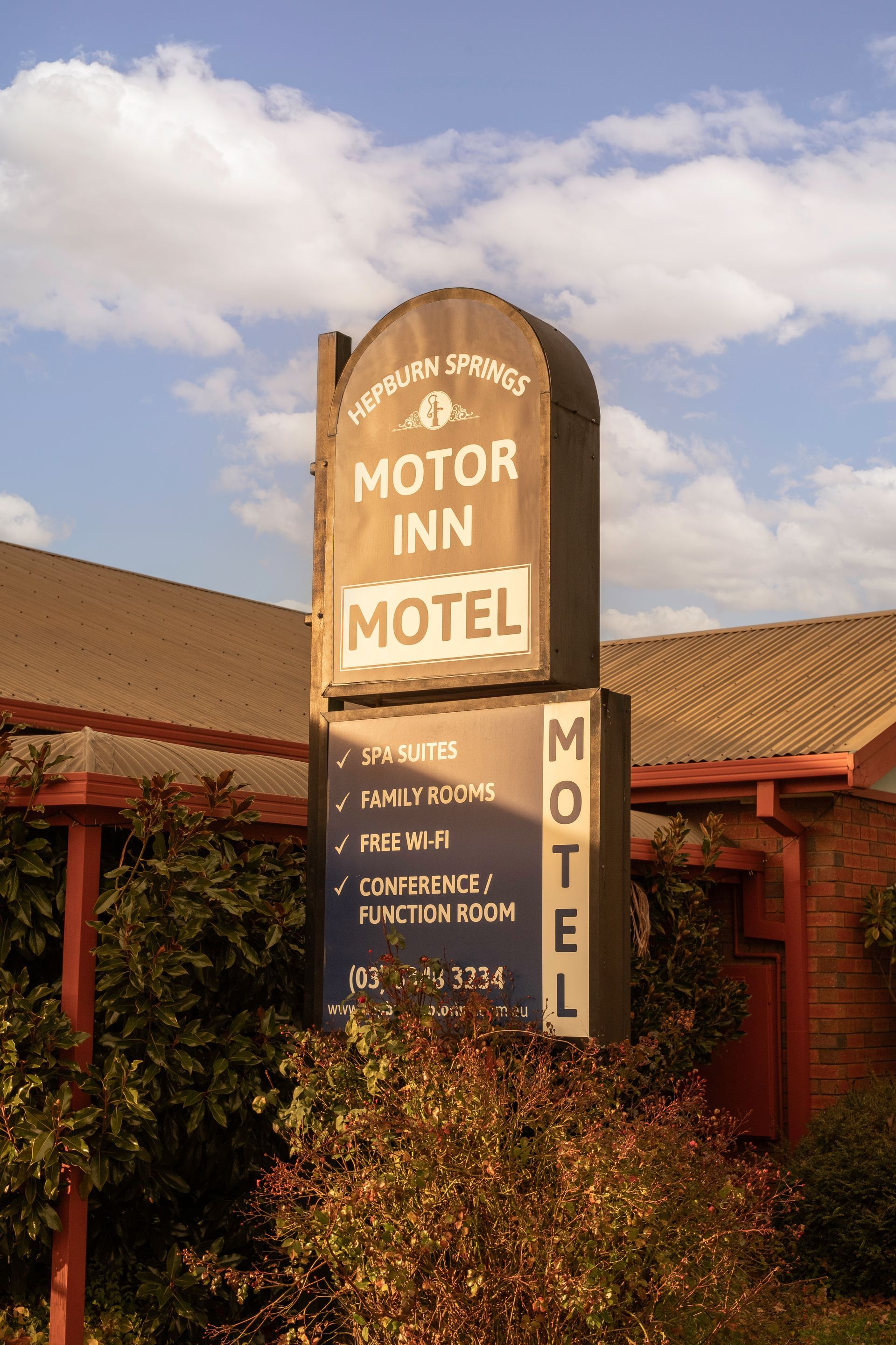 Motor Inn and Motel sign on a cloudy day, beige and blue with text. Building in background.