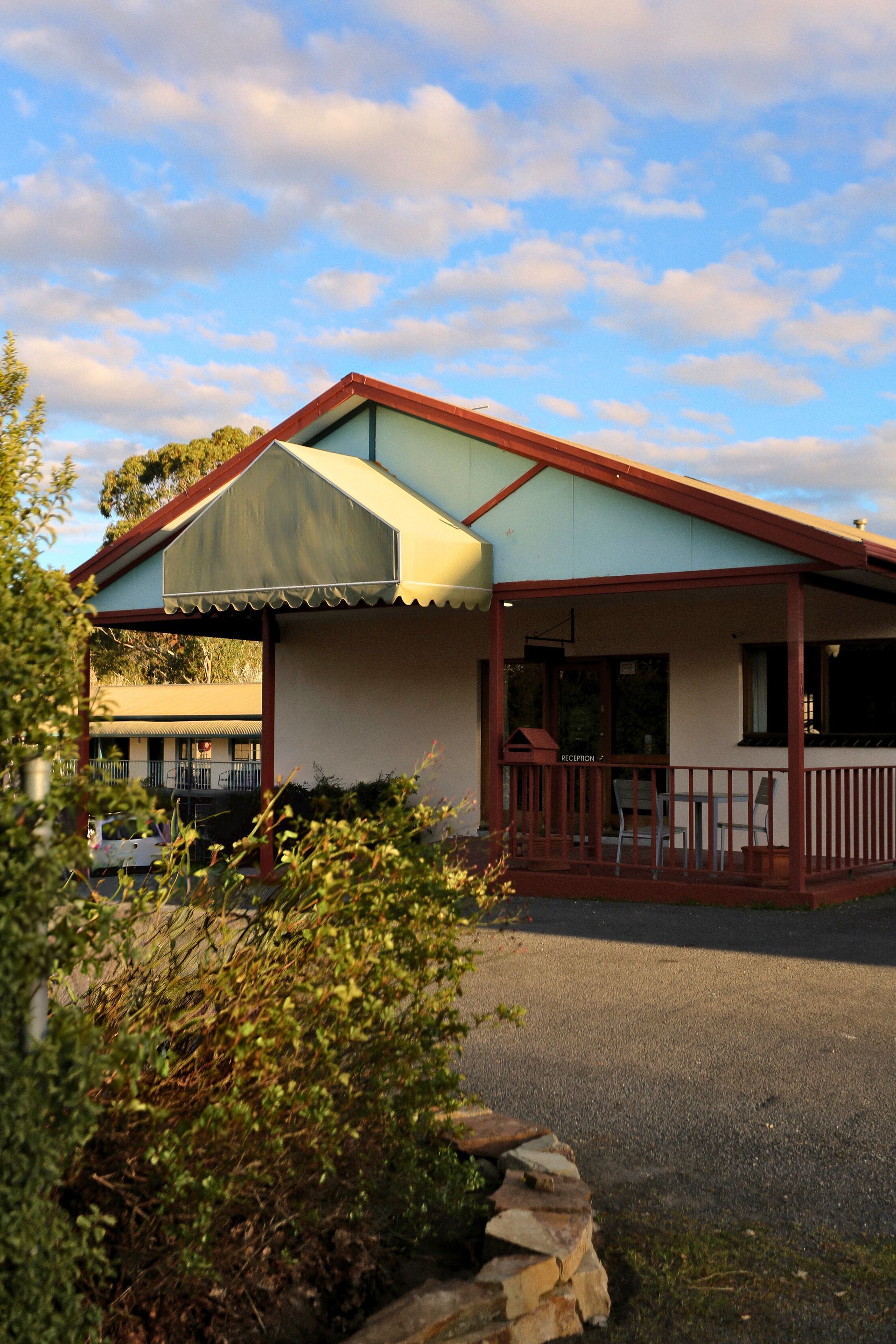 Cottage with light blue walls, brown trim, and a covered porch under a cloudy sky.