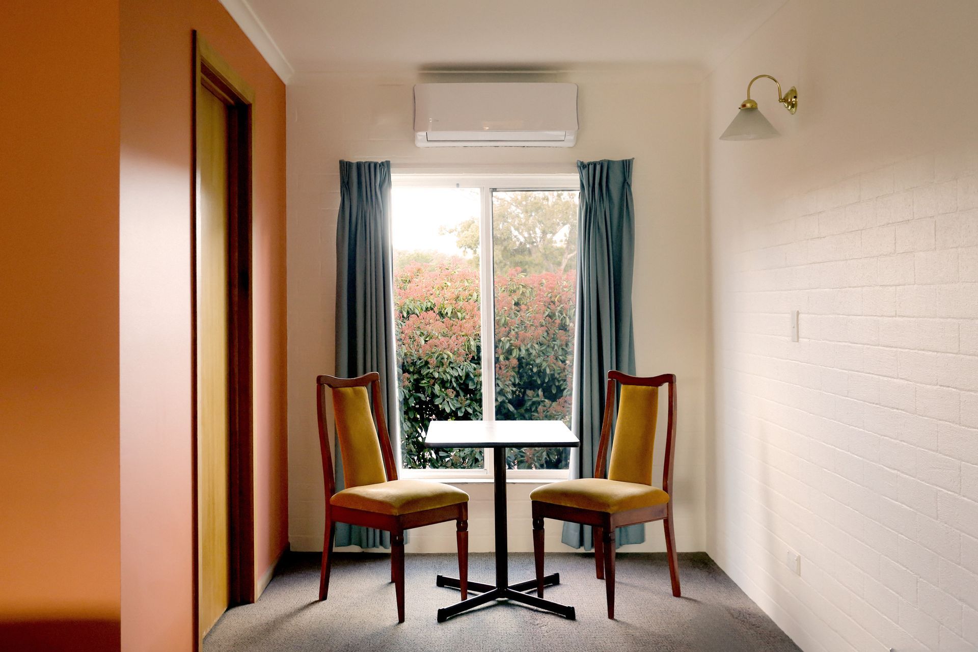 Two yellow-upholstered chairs face a small table by a window with blue curtains; inside a room.