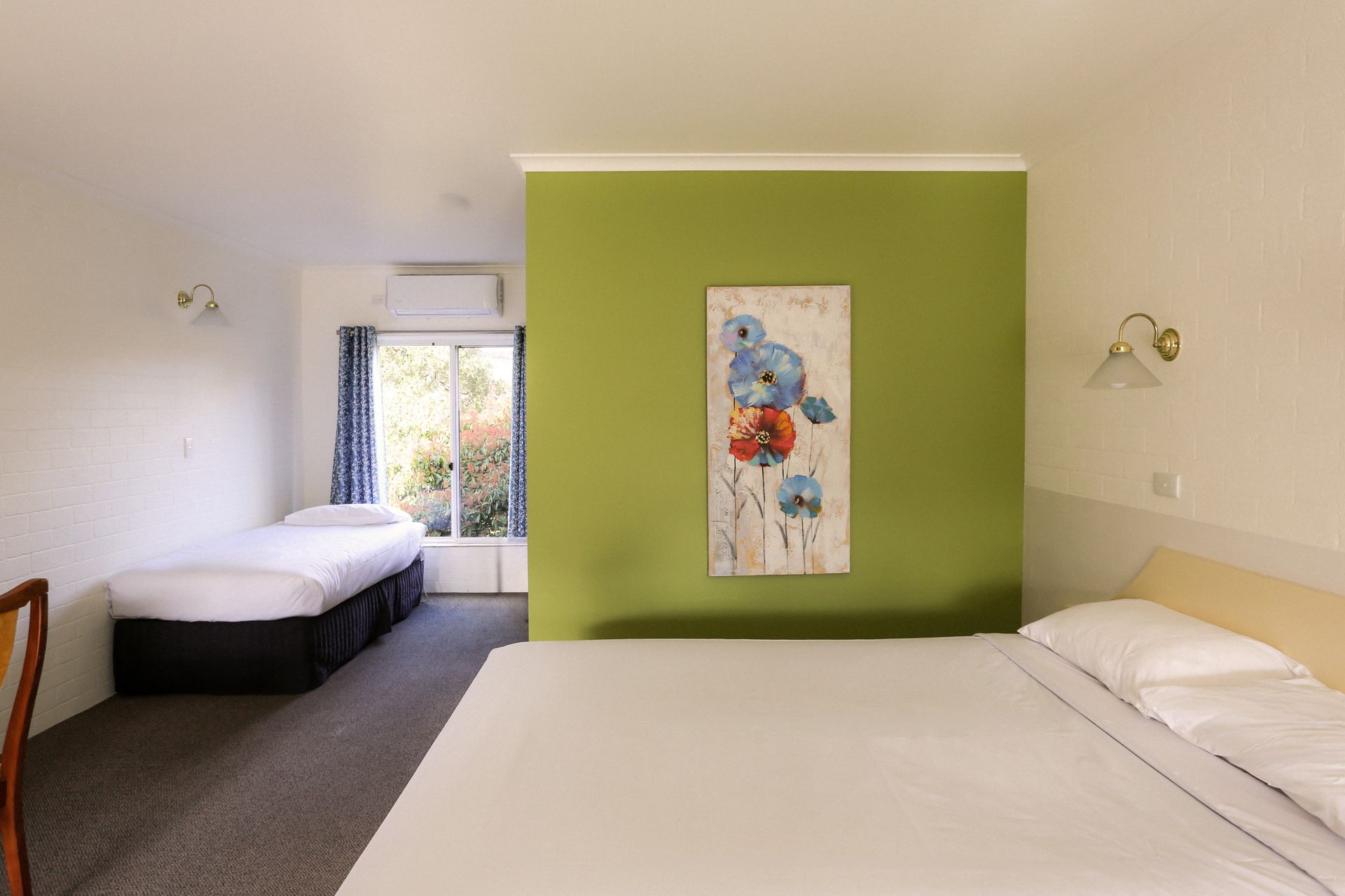 Motel room with double and single beds, green accent wall, floral art, and window.