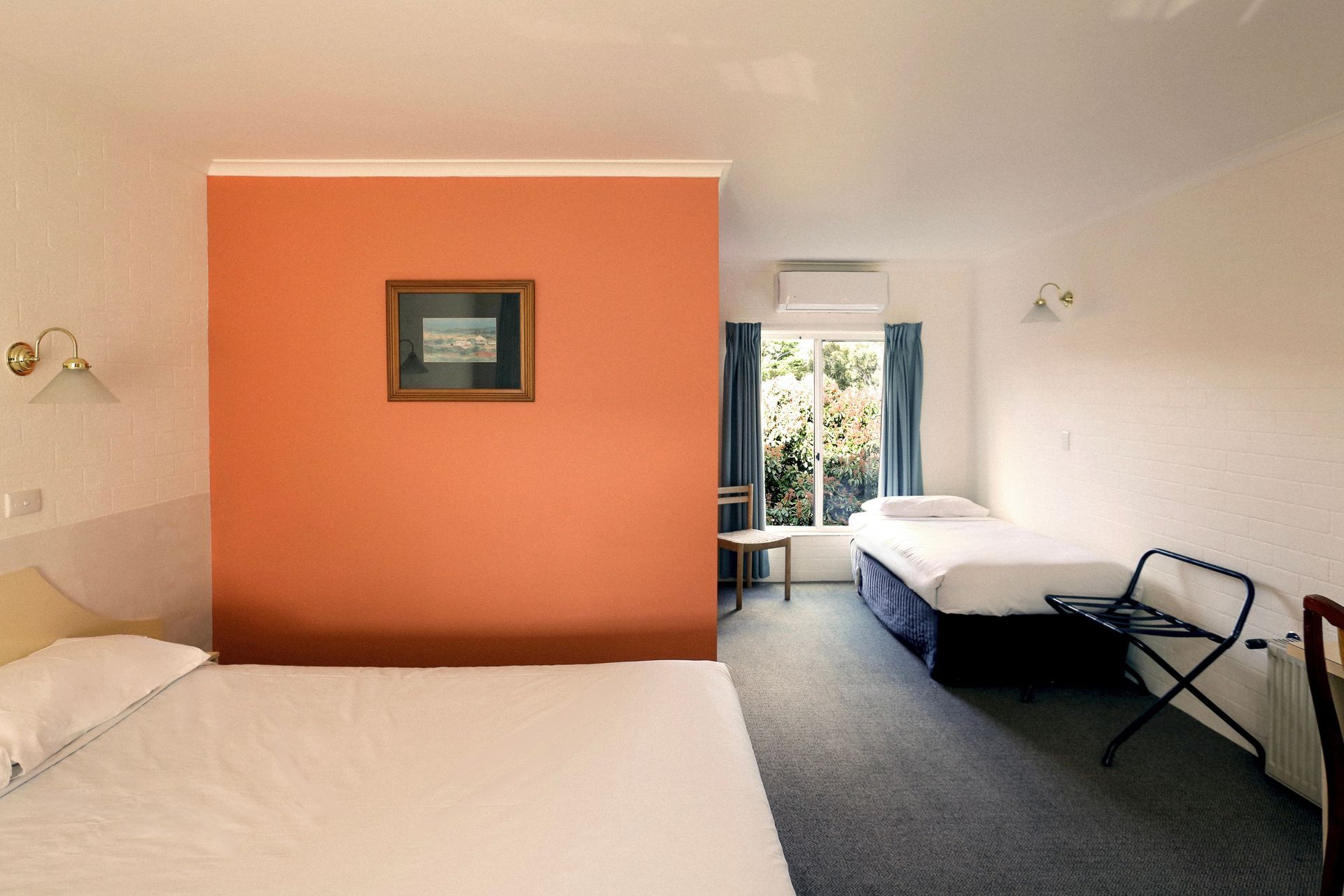 Hotel room with double and single beds, orange wall, and window with curtains.