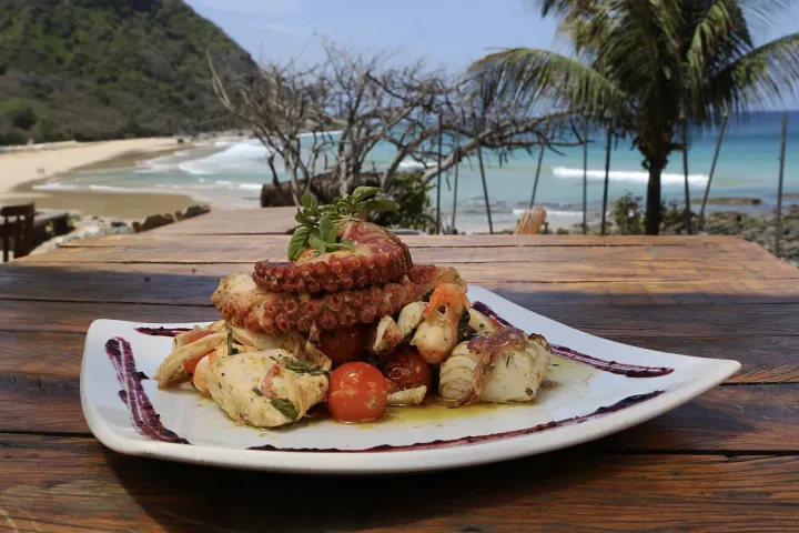 Um prato de comida está sobre uma mesa de madeira em frente à praia.