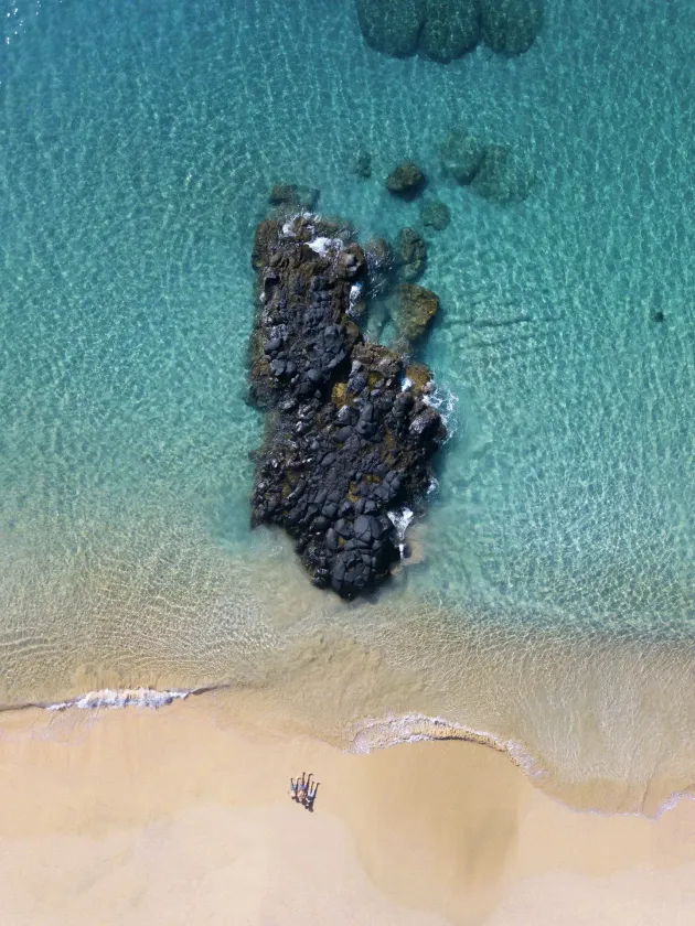 Uma vista aérea de uma praia com uma grande rocha no meio do oceano.