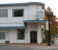 White two-story storefront with blue awnings and a sign, seen from the street in autumn.