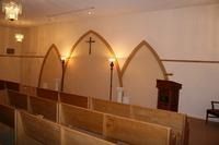 Church interior with wooden pews, arched partitions, a cross on the wall, and a pulpit