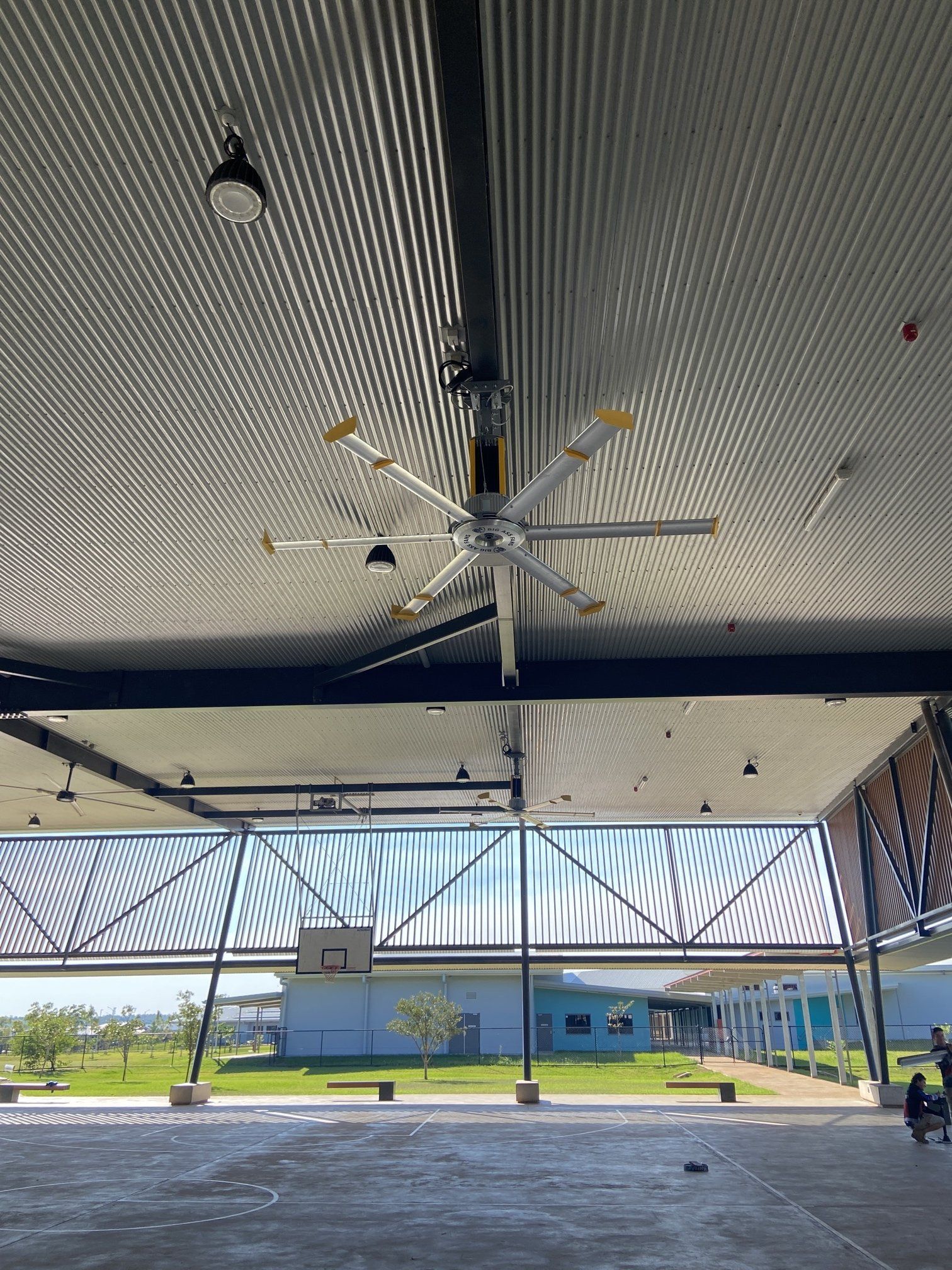 Open-air pavilion with metal roof, ceiling fans, and a blue building beyond the open side.