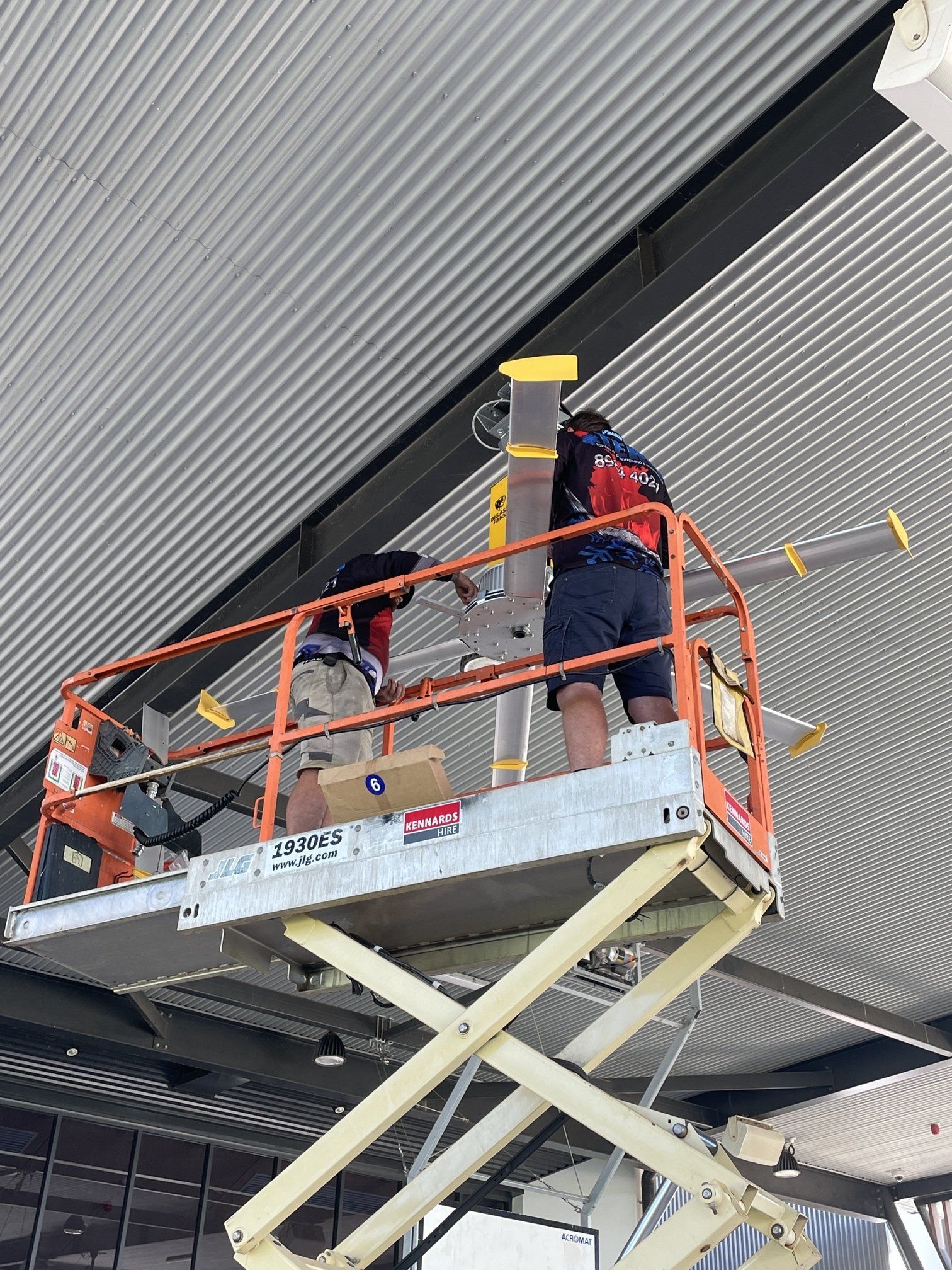 Workers on an orange scissor lift repairing the ceiling of a building