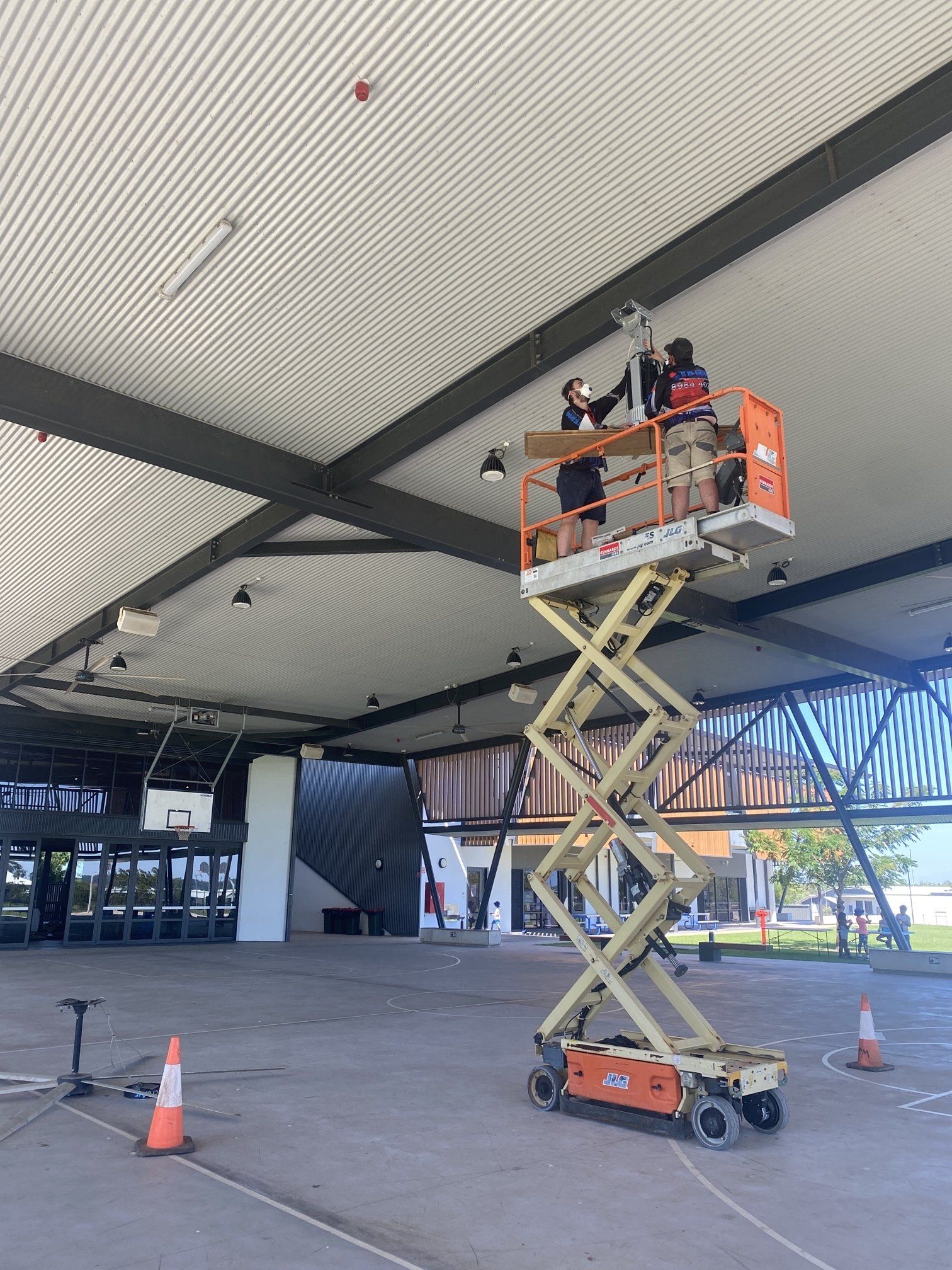 Two workers on a scissor lift inspecting the ceiling of a covered outdoor structure