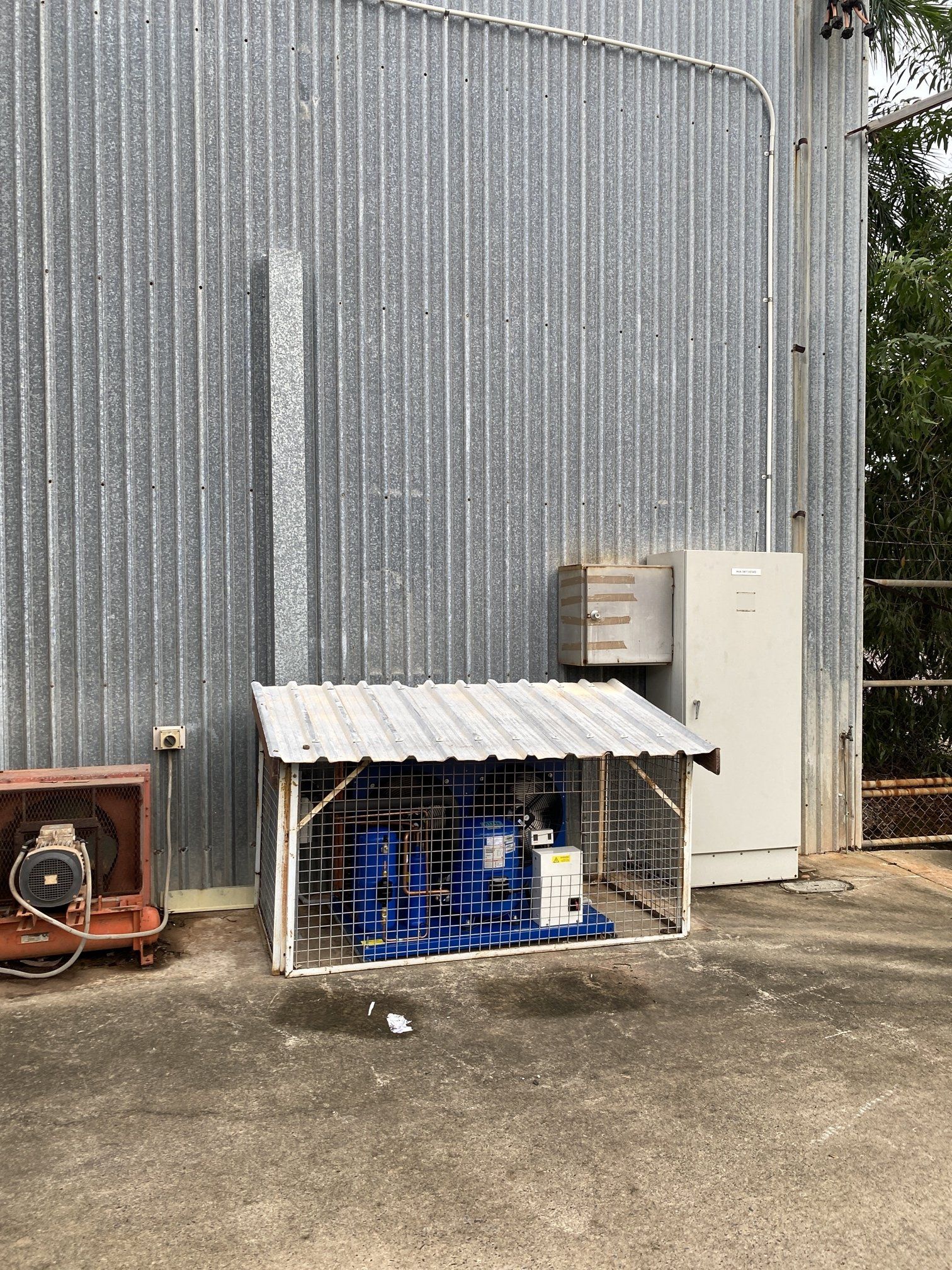 Blue bottles under a small corrugated shelter beside a gray metal building and outdoor utility units