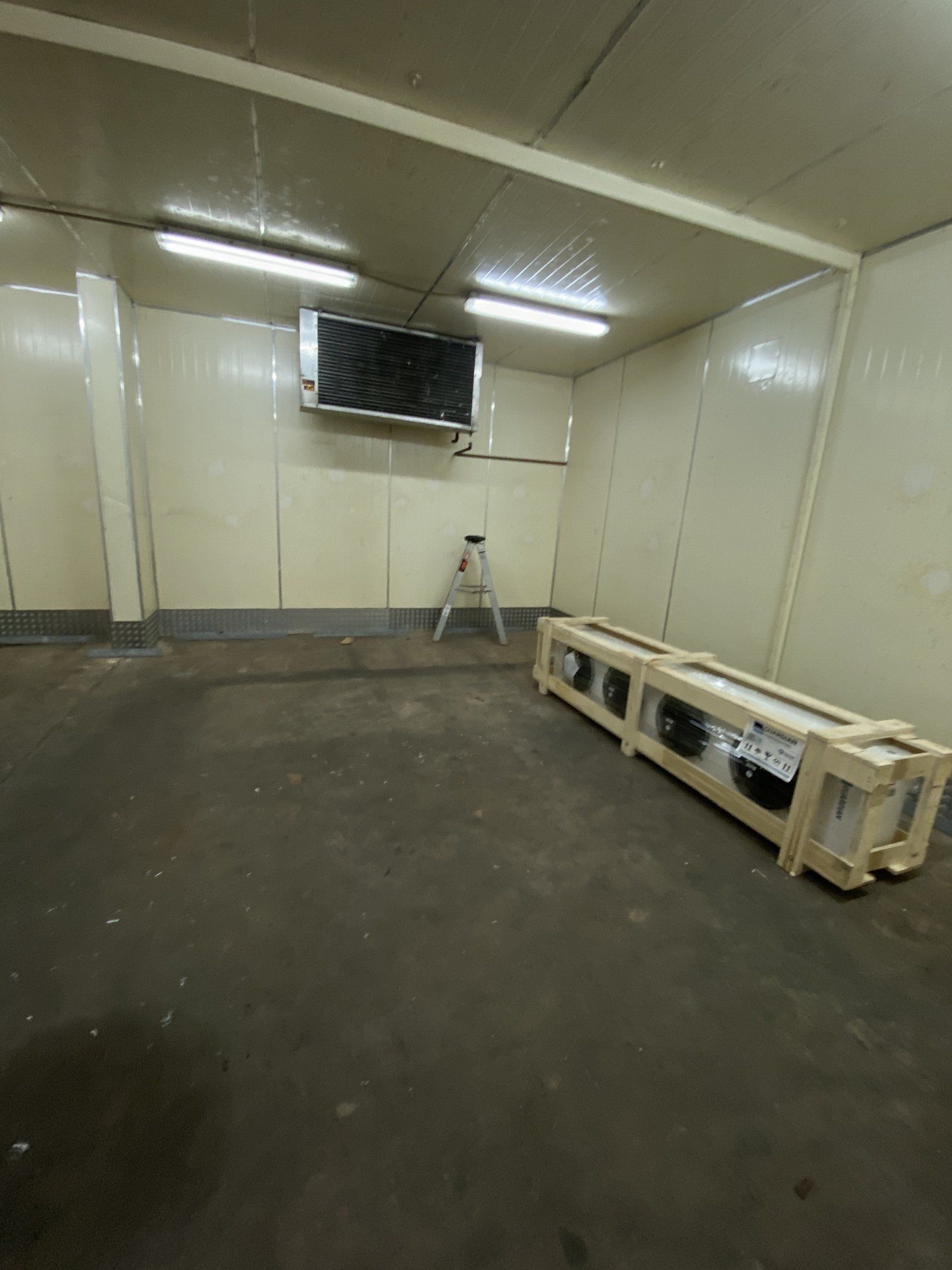 Empty industrial room with beige walls, a stool, and a wooden bench along the right wall